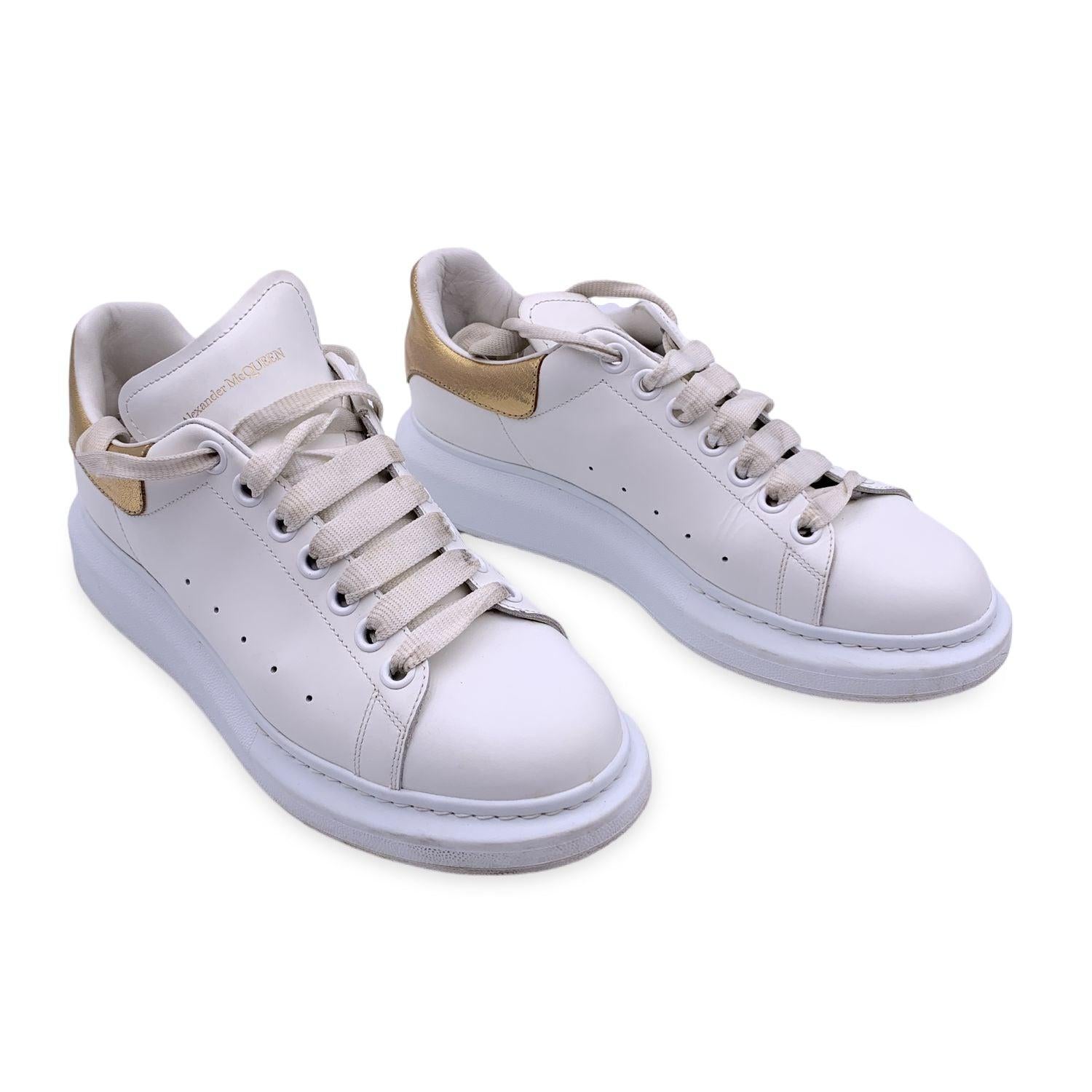 White sneakers in smooth shiny calfskin by Alexander McQueen. They feature laces, round oversized rubber toe and gold metal details on the back. Perforated finish on the outside. Leather lined interior. 7 metal holes. Flat laces. Alexander McQueen