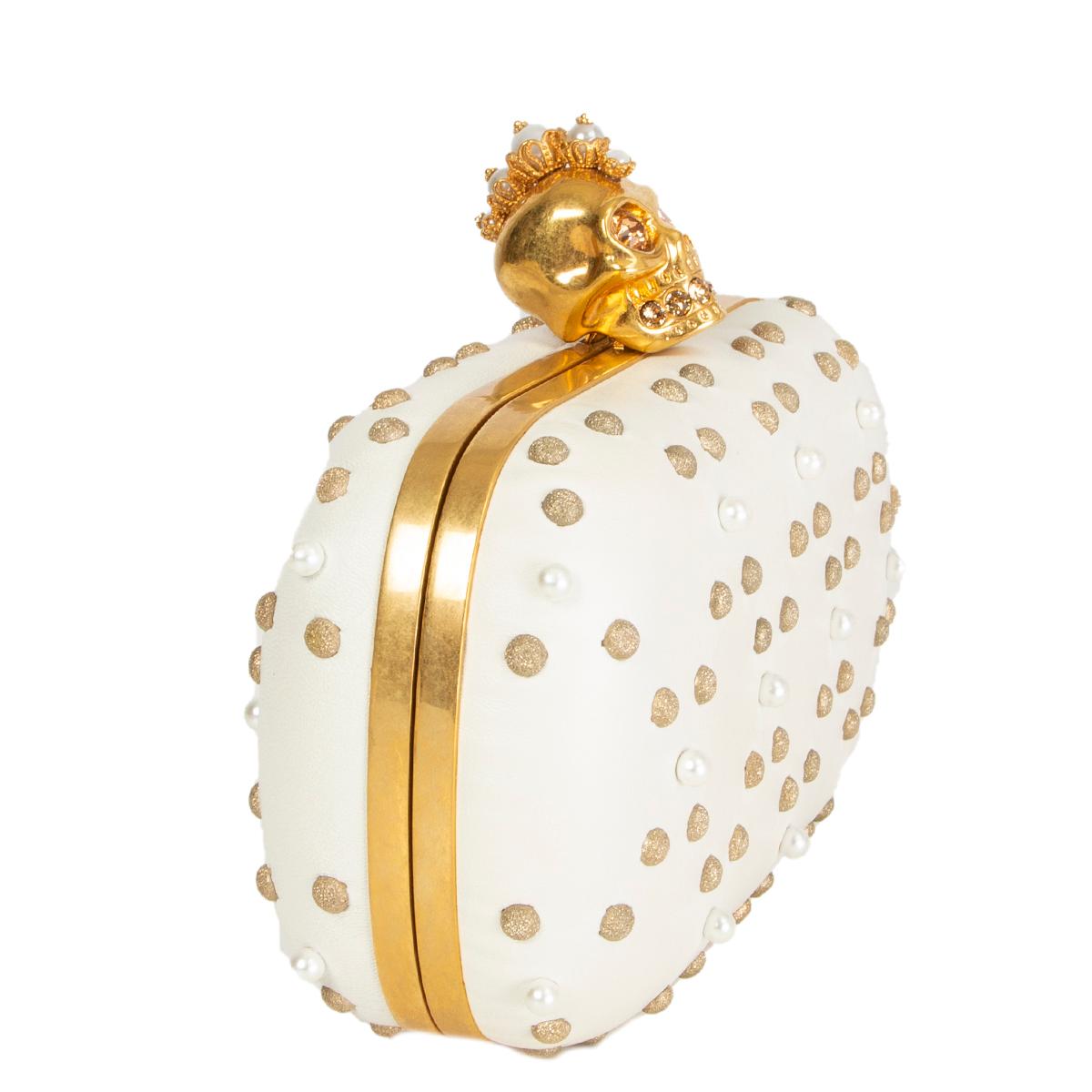 Alexander McQueen skull box clutch in off-white lambskin embellshed with pearls and light gold-tone studs featuring gold-tone metal skull closure with crystal eyes and teeth. Lined in off-white calfskin. Has been carried with one missing pearl on