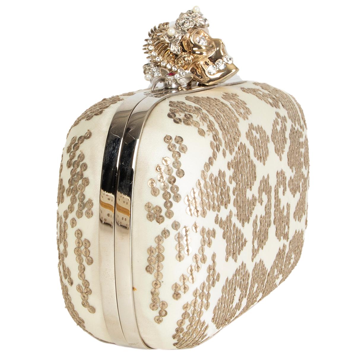 Alexander McQueen skull box clutch in off-white satin embellshed with antique silver-tone sequins and light gold-tone skull closure with crystal eyes and teeth. Lined in off-white calfskin. Has been carried with some oft discoloration on the buttom.