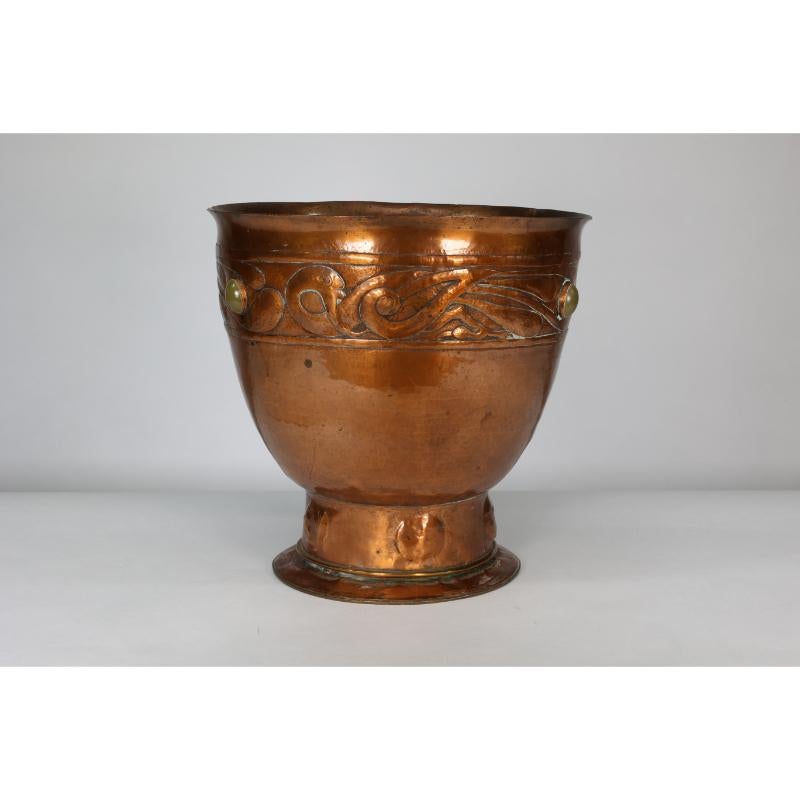Estilo Alexander Ritchie de Iona. Gran maceta de cobre de grueso calibre, martillada a mano, con dragones celtas cincelados alrededor de la parte superior e incrustados con ojos de buey de cristal, sobre una base entallada con decoración circular y