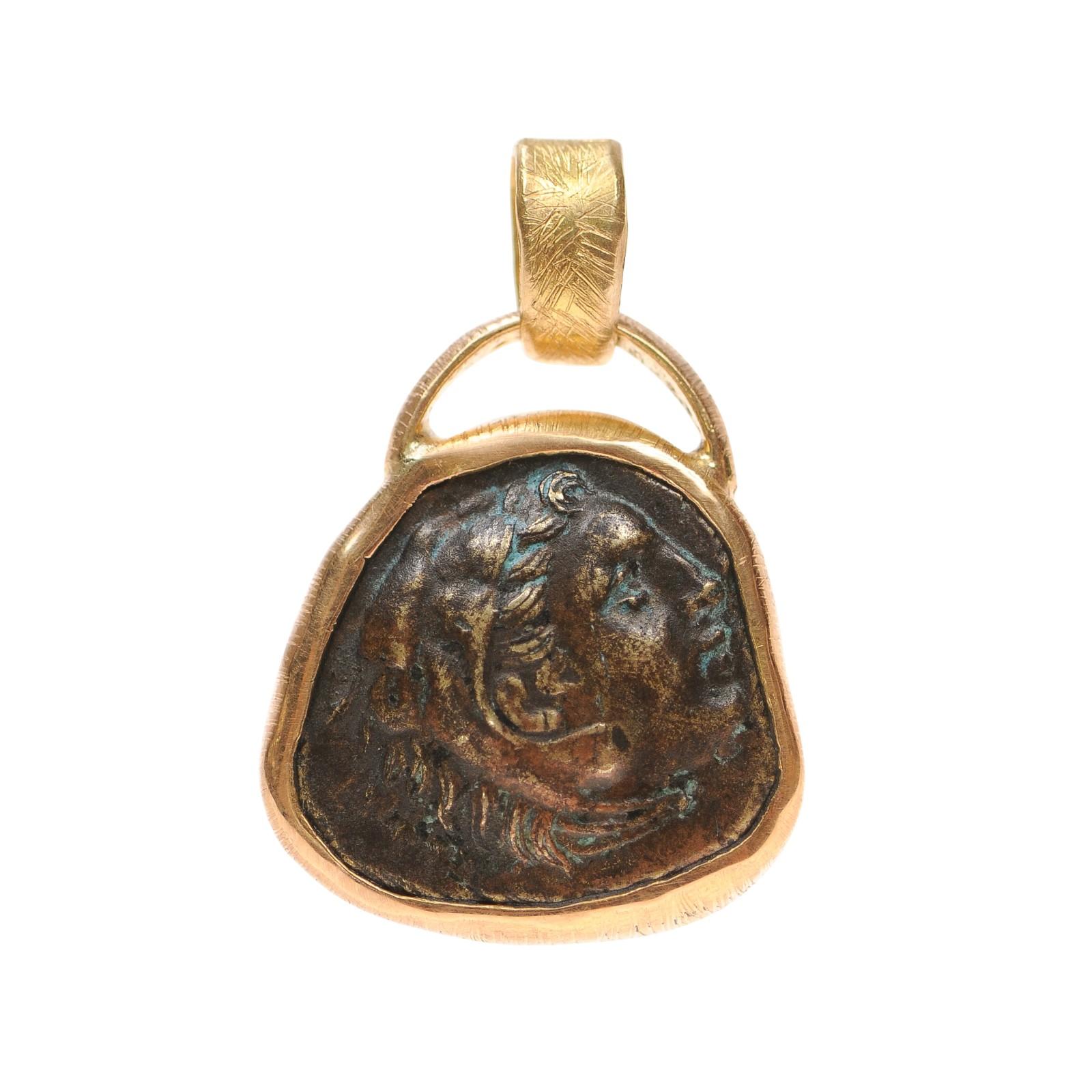 A bronze coin pendant of Alexander the Great, minted circa 336-323 B.C., trimmed with 22 karat gold. On the obverse side of this coin is Heracles wearing lions skin. On the reverse side, Hercules with a bow and arrow, with quiver and club, above.