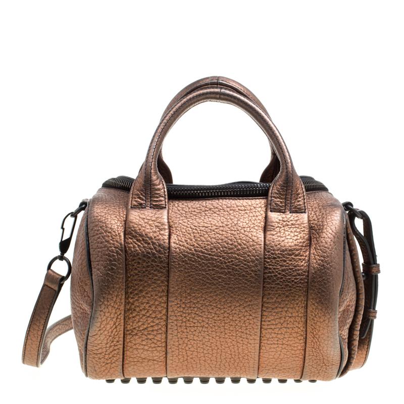 Creations like this Rocco bag by Alexander Wang never go out of style. This bronze textured bag is crafted from pebbled leather and it features dual handles, a detachable shoulder strap, and studs on the bottom. The top zipper opens to a nylon