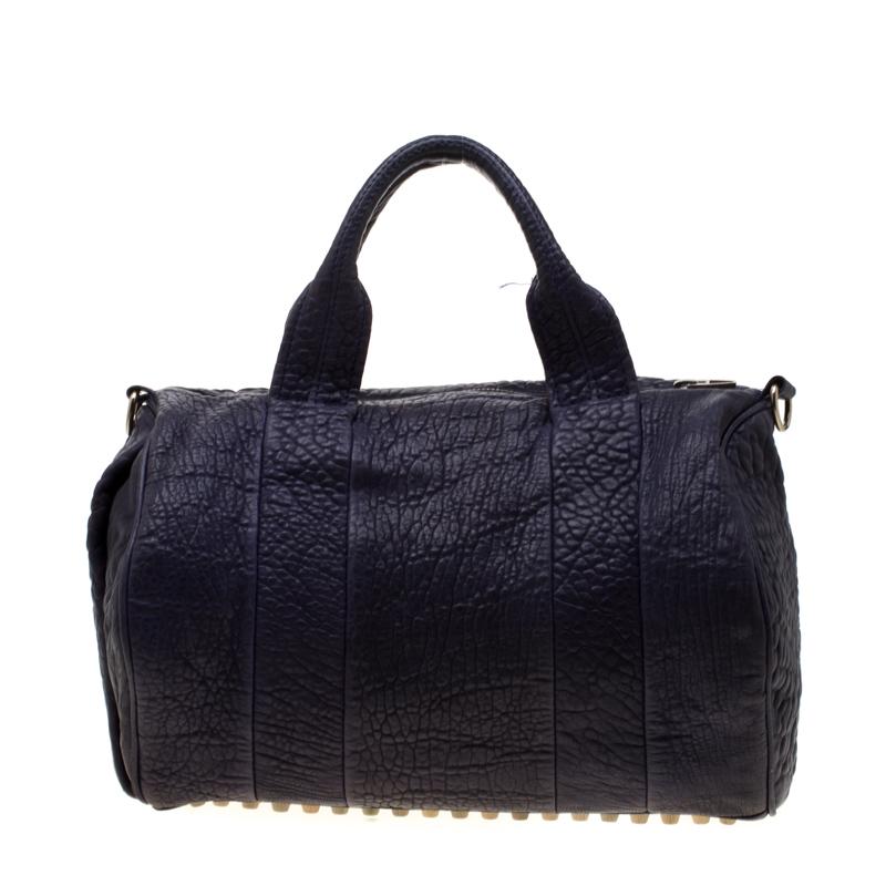 Creations like this Rocco Duffle Bag by Alexander Wang never go out of style. This purple bag is crafted from pebbled leather and it features dual handles, a detachable shoulder strap, and studs on the bottom. The top zipper opens to a fabric
