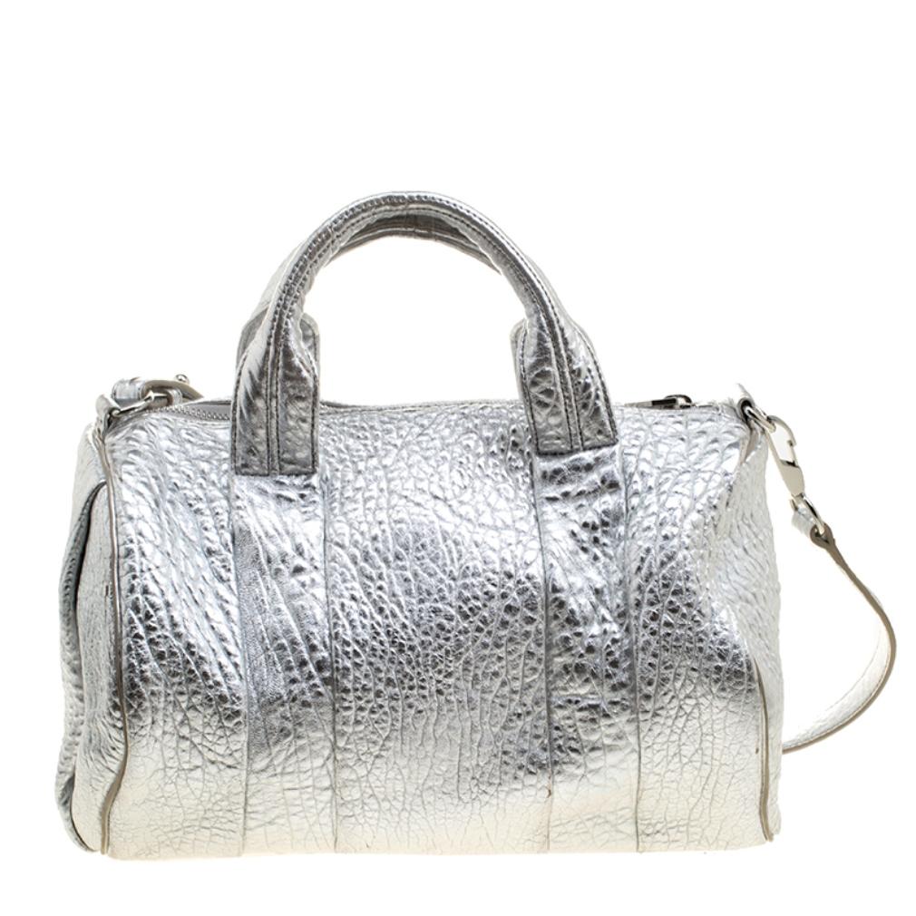 Creations like this Rocco Duffle Bag by Alexander Wang never go out of style. This silver bag is crafted from pebbled leather and it features dual handles, a detachable shoulder strap, and studs on the bottom. The top zipper opens to a fabric