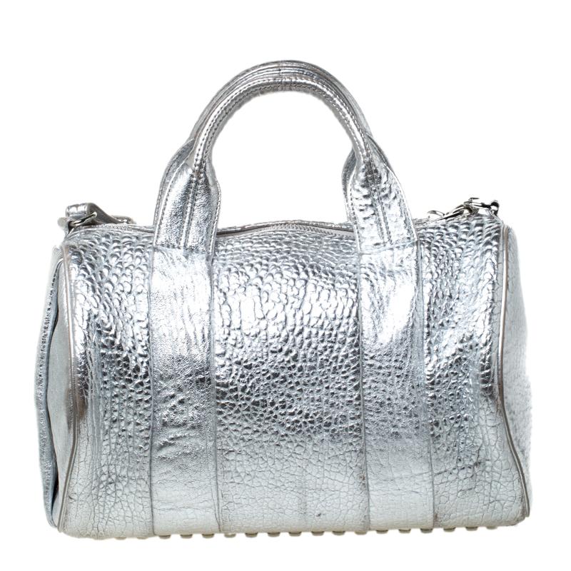 Creations like this Rocco Duffle Bag by Alexander Wang never go out of style. This silver bag is crafted from pebbled leather and it features dual handles, a detachable shoulder strap, and studs on the bottom. The top zipper opens to a fabric