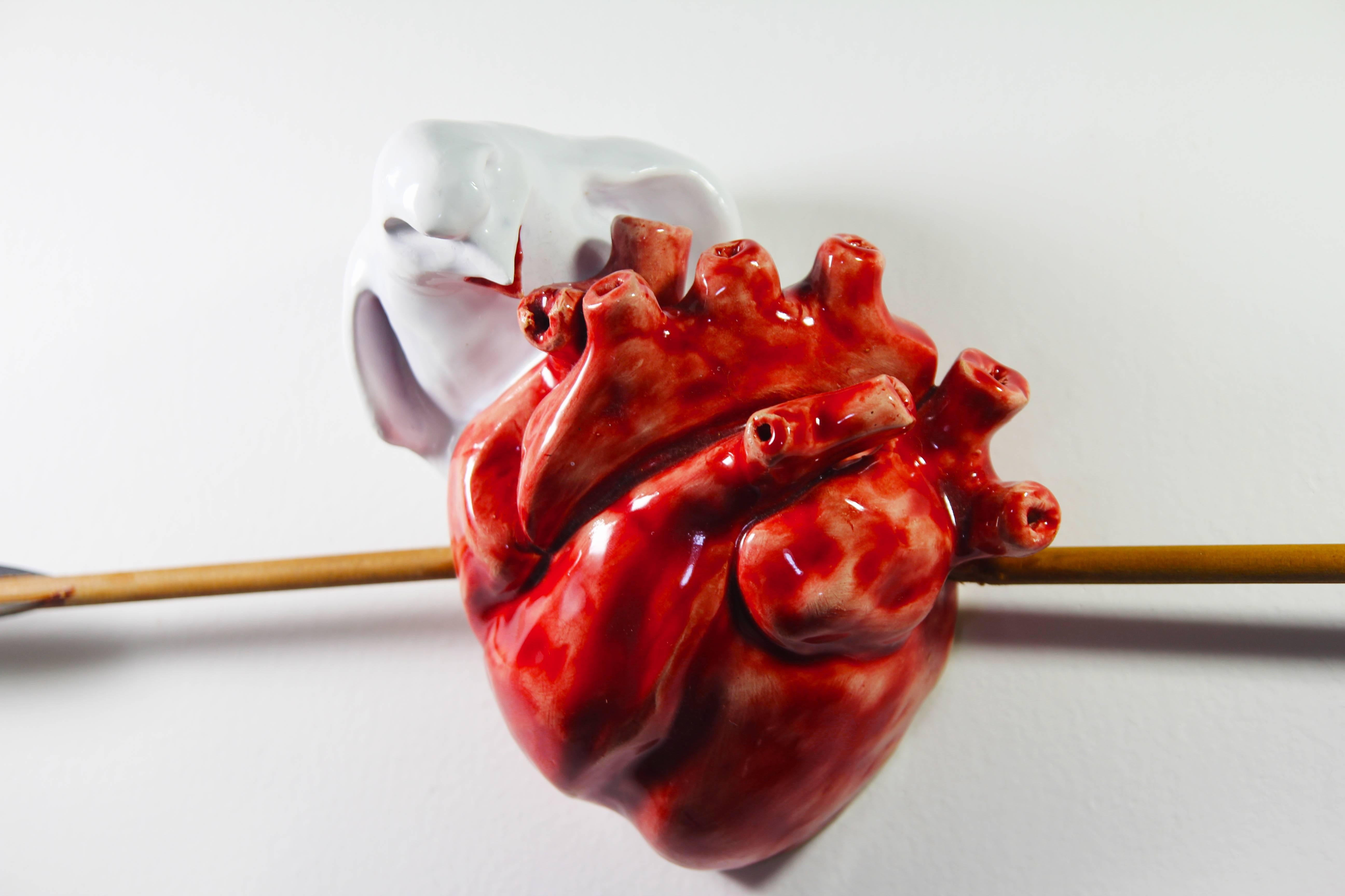 Heart in ceramic, glazed in red color. Contains real wooden arrows. 
The creation shows a white Bird eating a red fresh still alive beating  heart, with an arrow running through it. 
It represents comings and goings of love.