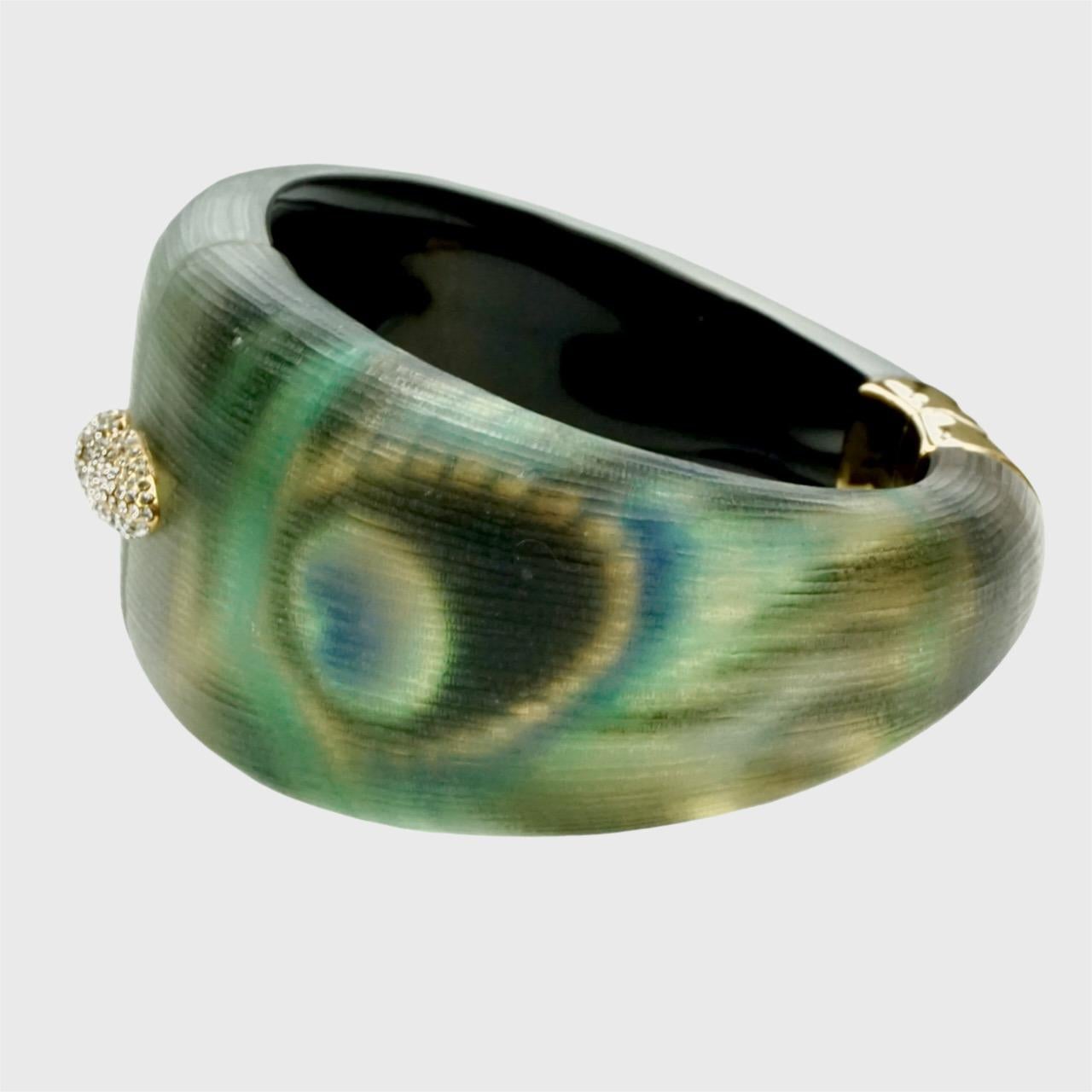 Precioso brazalete de plumas de pavo real de lucite texturizado de Alexis Bittar con un detalle de brillantes. Tiene una bisagra chapada en oro y un cierre magnético.

Mide un diámetro interior de 6,4 cm por 5,1 cm. La anchura del brazalete es