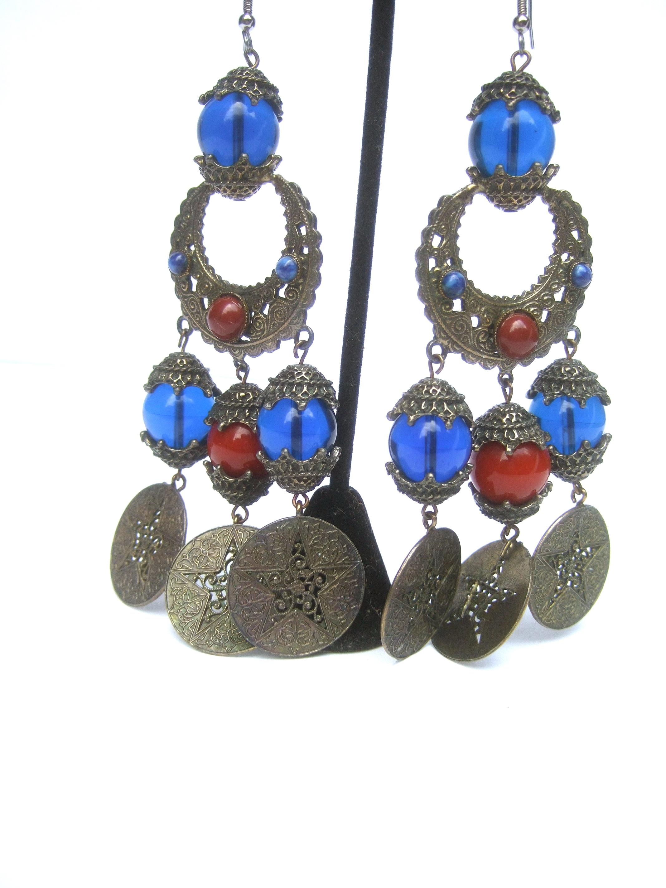 Alexis Kirk Massive Etruscan style glass beaded dangling charm statement earrings c 1970s
The ornate burnished brass metal designer pierced runway mogul style earrings 
are embellished with glass beads in translucent cobalt blue color glass beads