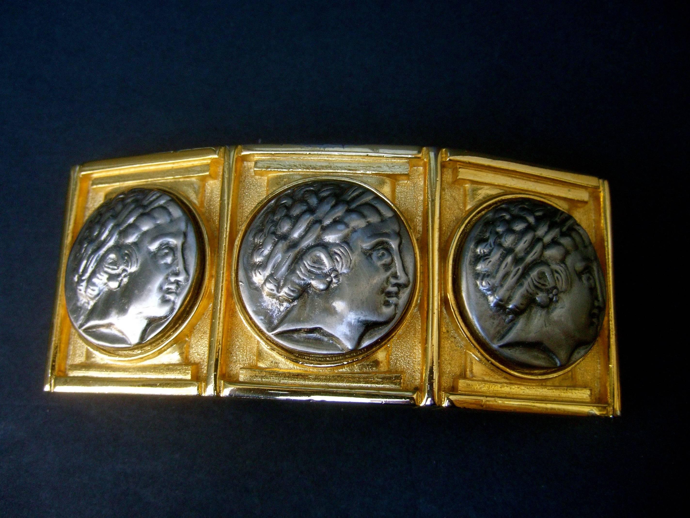 Alexis Kirk Boucle de ceinture massive en métal doré avec médaillon romain, datant des années 1980
La boucle de ceinture unique à l'échelle gigantesque est ornée d'un trio 
de médaillons à tête figurative de style romain en métal de couleur