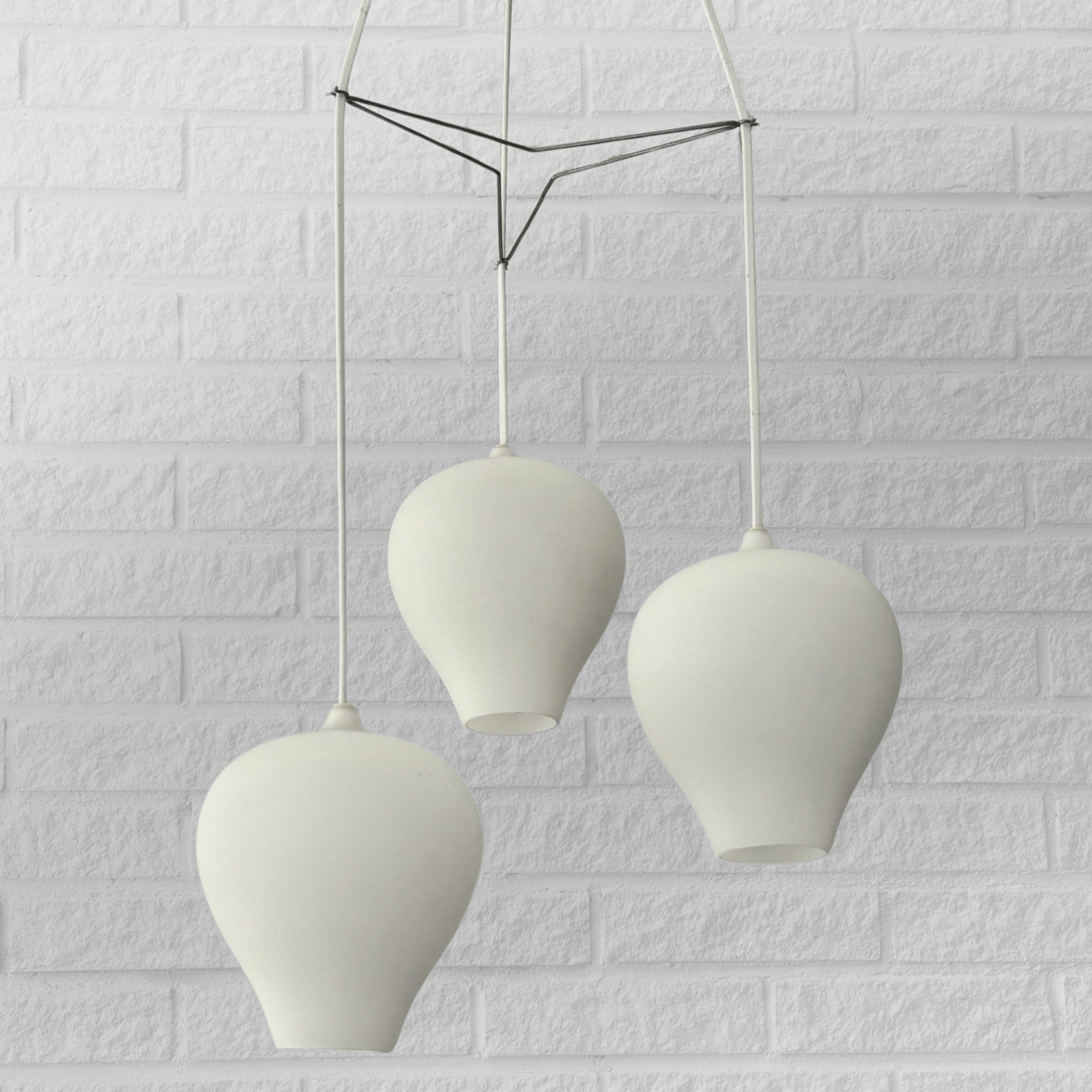 An eye-catching pendant lamp designed by Alf Svensson for the renowned Swedish lighting manufacturer Bergboms in 1953. This exquisite design features a minimalist aesthetic, with three clock-shaped opal glass shades interconnected by a metal wire