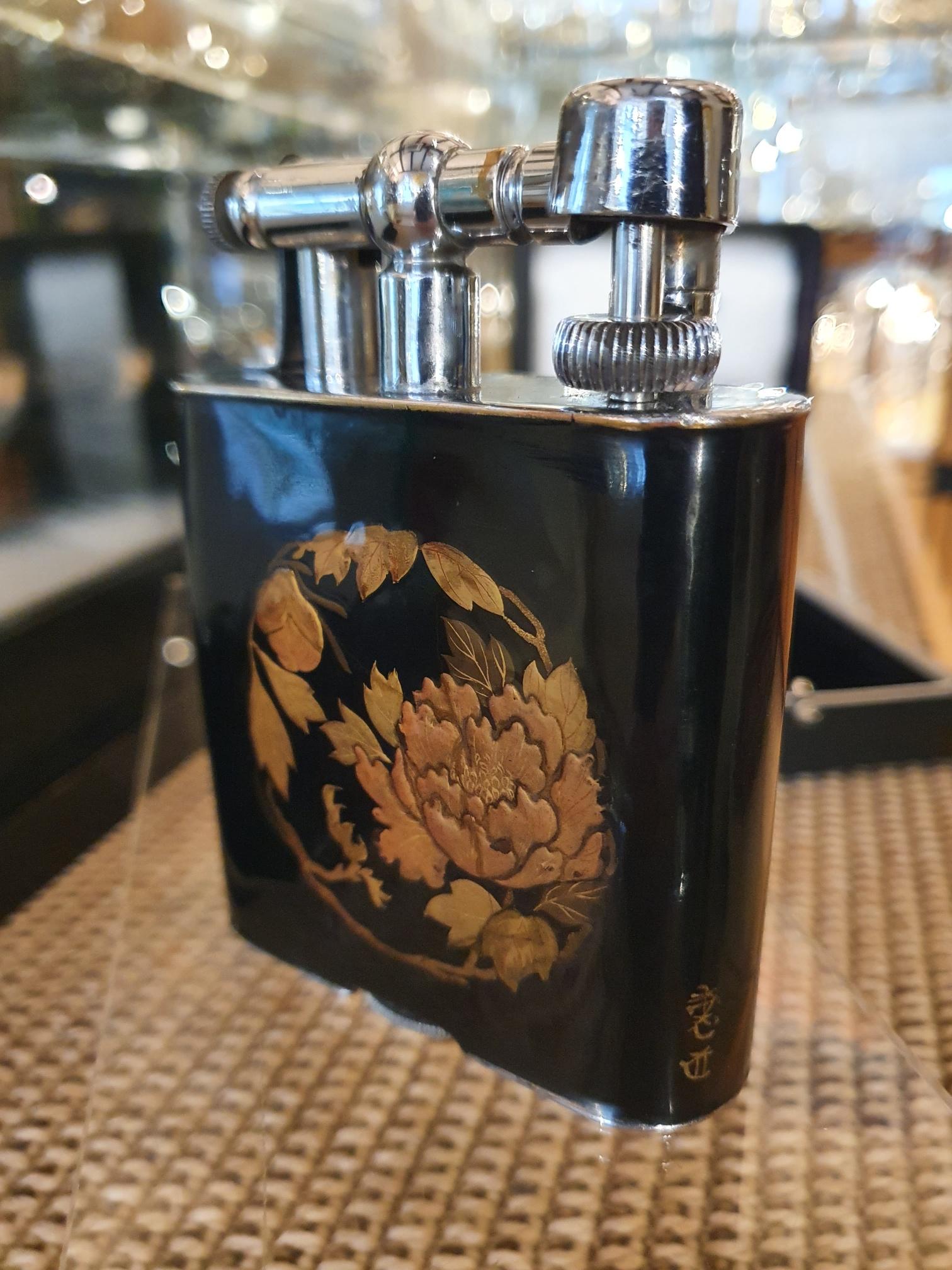 Alfred Dunhill, London

A scarce Dunhill ‘Namiki’ maki-e enamel table lighter with chrome-plated hardware, with a glossy black lacquer background and circular design of a Chrysanthemum with foliage to the front, and a design of grapes and vines to