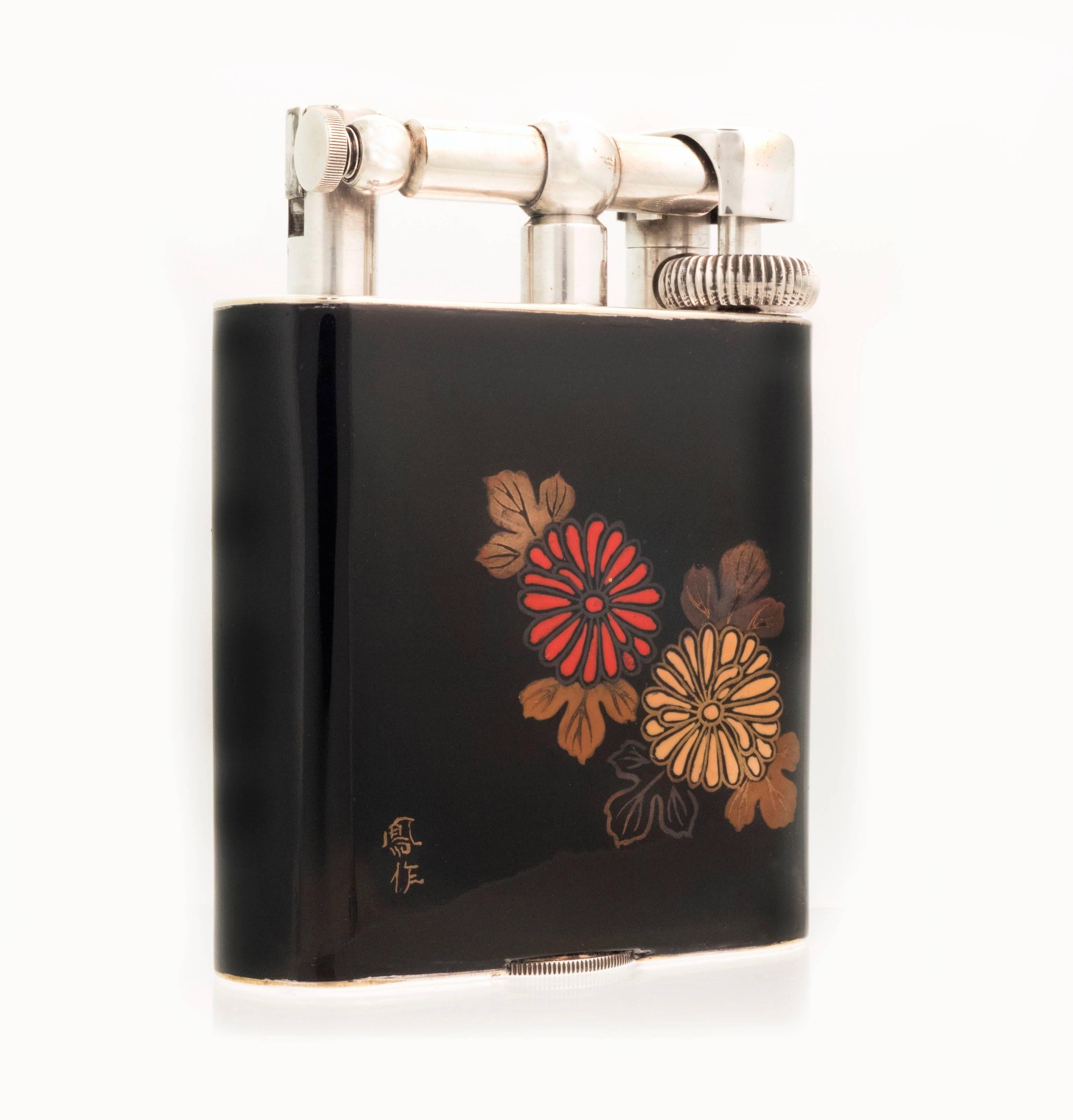 An extremely scarce ‘Namiki’ table lighter in ‘Giant’ table size with silver-plated hardware with a glossy black background with a red and yellow chrysanthemum with foliage to the front, and three gold and red flowers with foliage to the reverse.