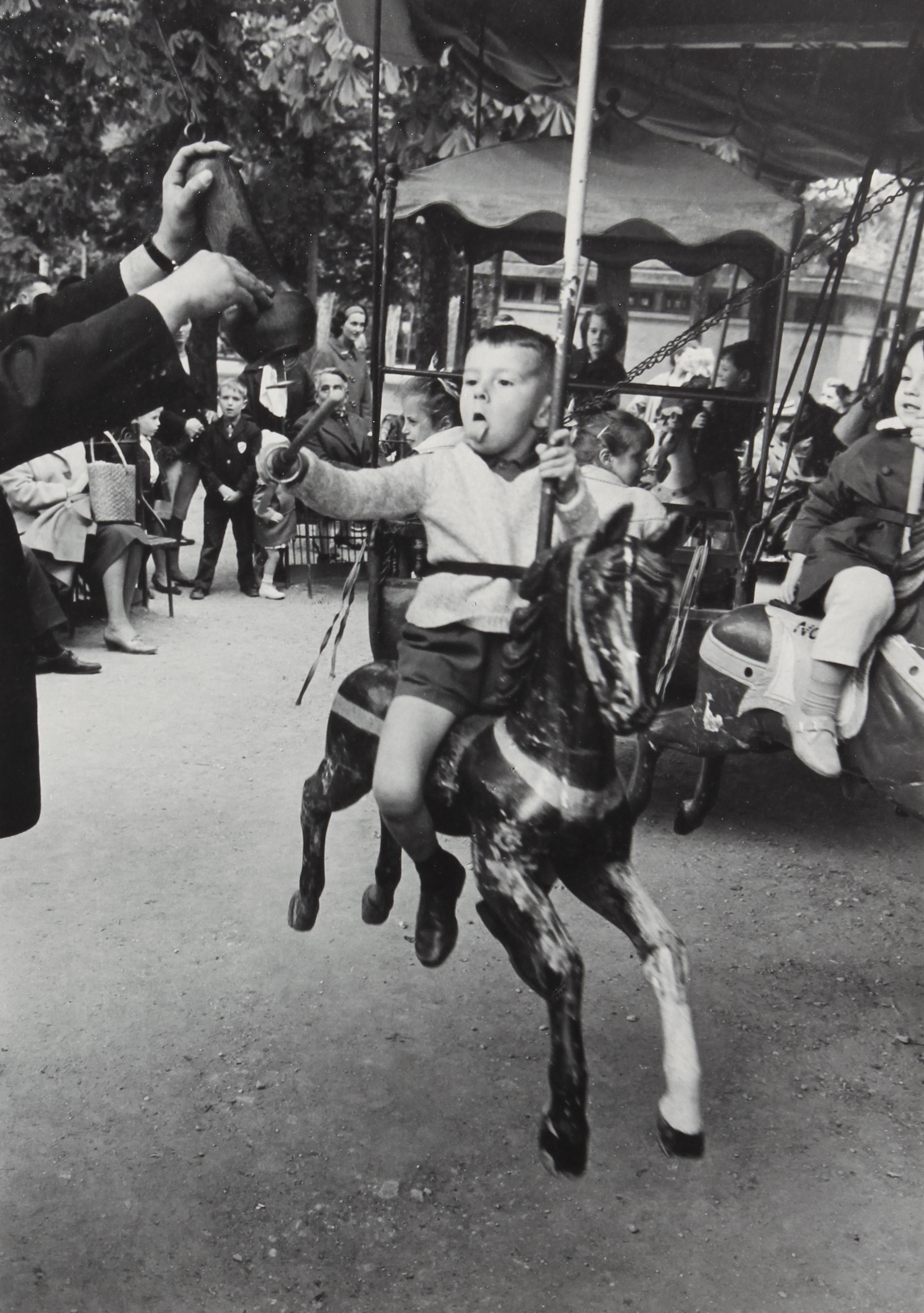 Alfred Eisenstaedt Black and White Photograph - Boy with Tongue Out Spearing Brass Ring, Luxembourg Garden, Paris 