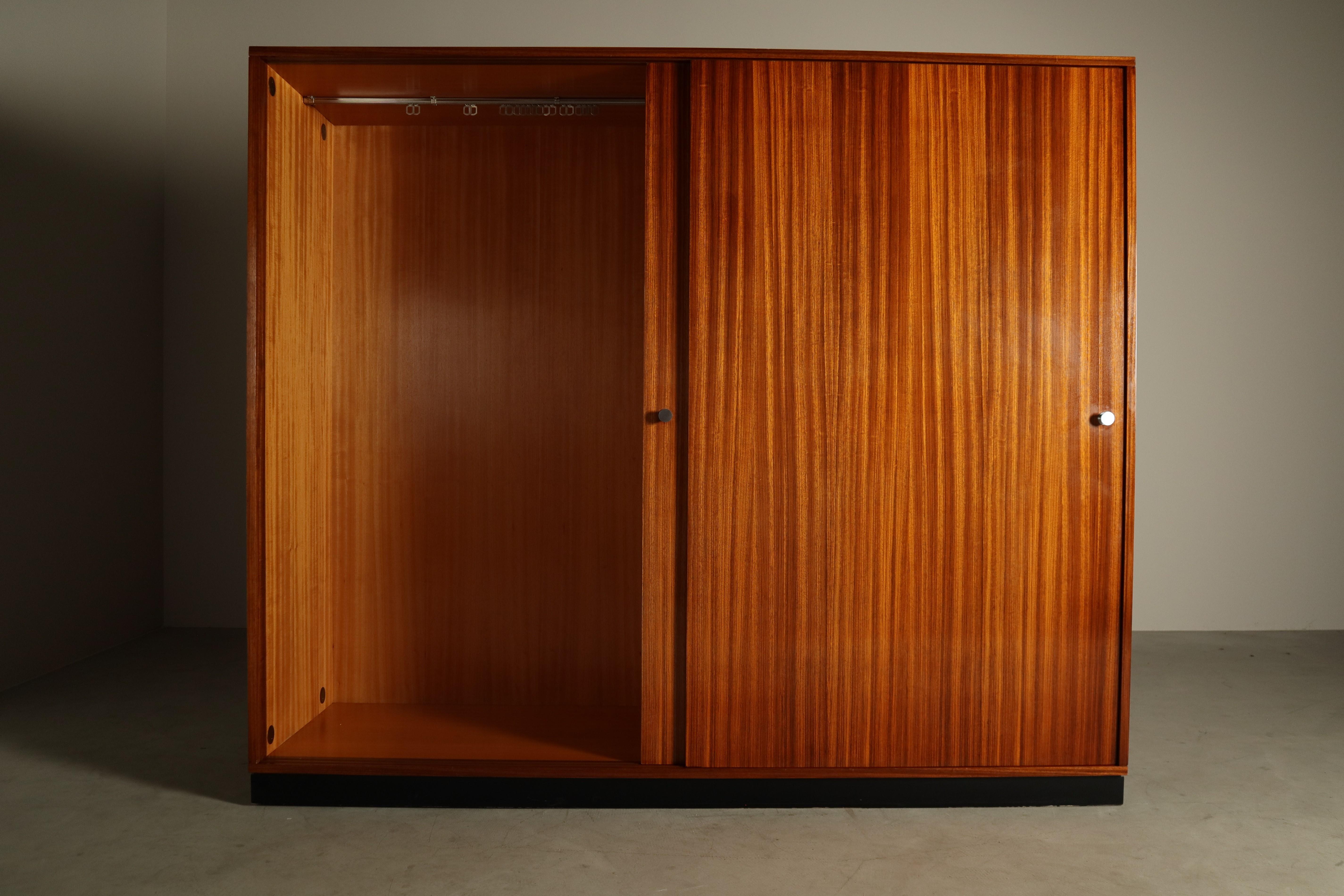 Elegante armario de puertas correderas de mediados de siglo, de Alfred Hendrickx para Belform (Bélgica). Acabado en llamativa chapa de cebrano, con puertas correderas a juego con el libro que resaltan el fuerte veteado vertical. Los detalles