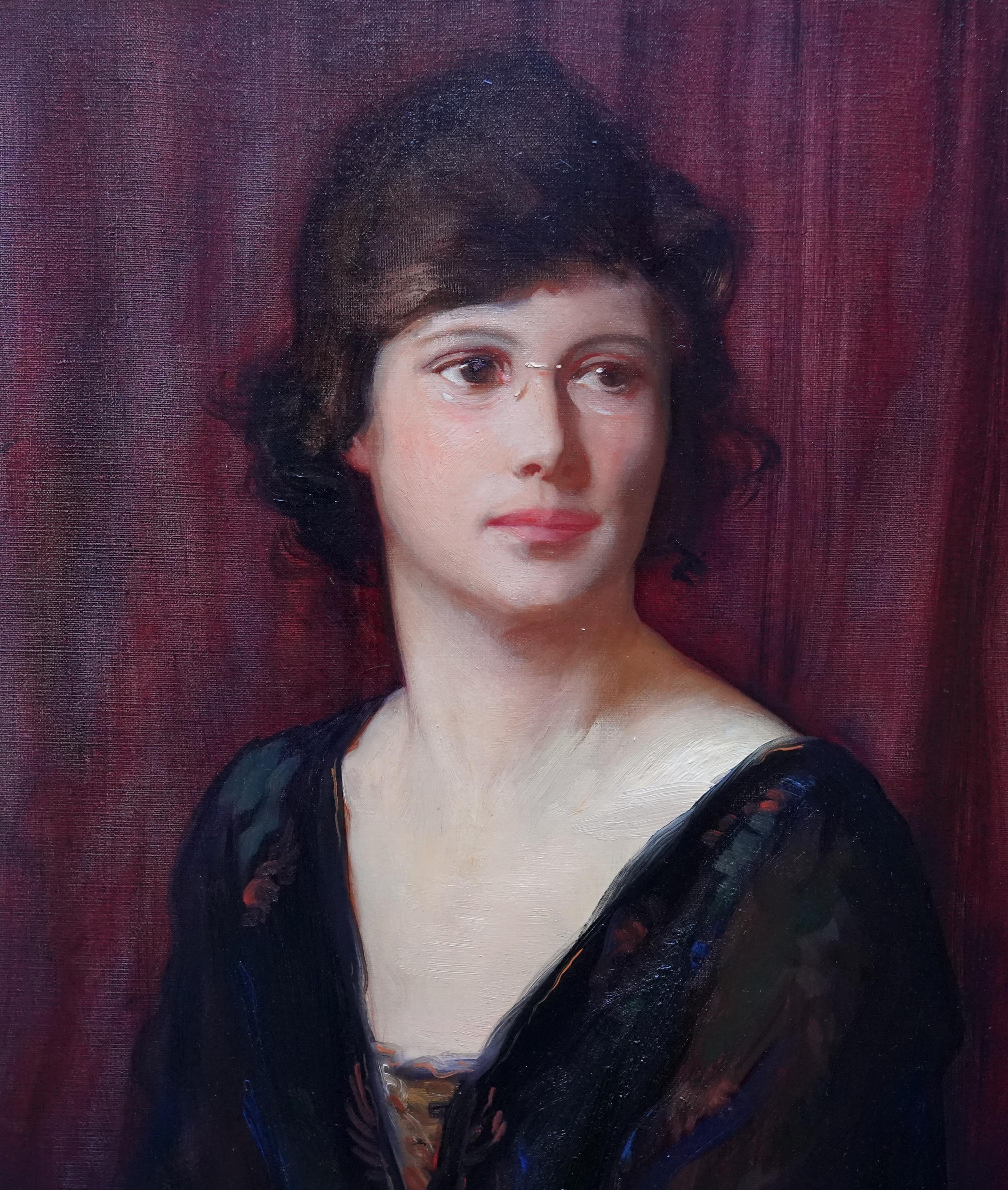 This superb British portrait oil painting is by noted artist Alfred Kinglsey Lawrence. Painted in 1919 it is a seated portrait of a young woman with a lush burgundy velvet curtain behind her that really zings in colour. She is wearing a black lace