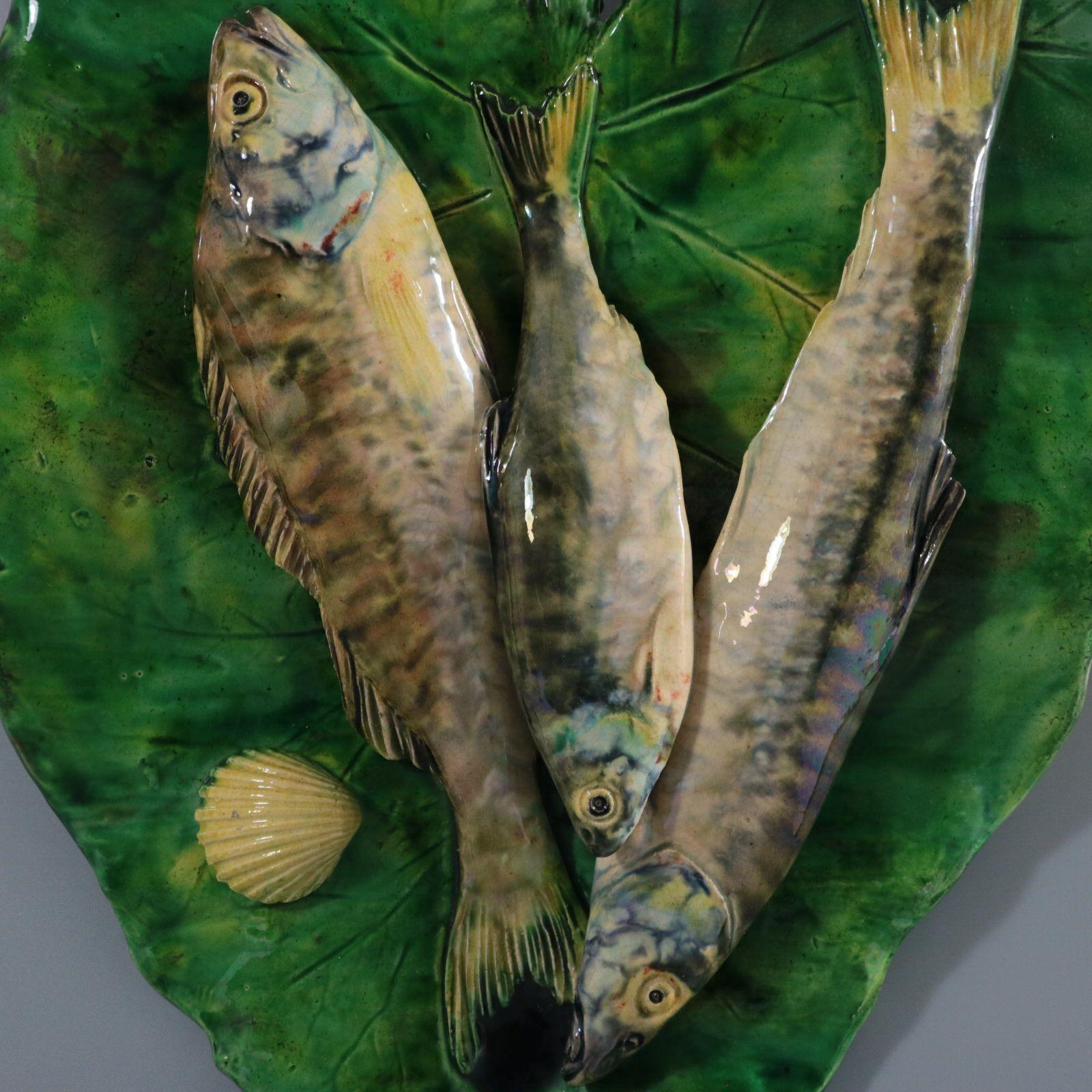 Wandtafel aus französischer Palissy-Majolika von Alfred Renoleau, auf der drei sich überlappende Fische auf einem großen Blatt abgebildet sind. Färbung: Grün, grau, cremefarben, sind vorherrschend. Das Stück trägt die Herstellermarken der Töpferei