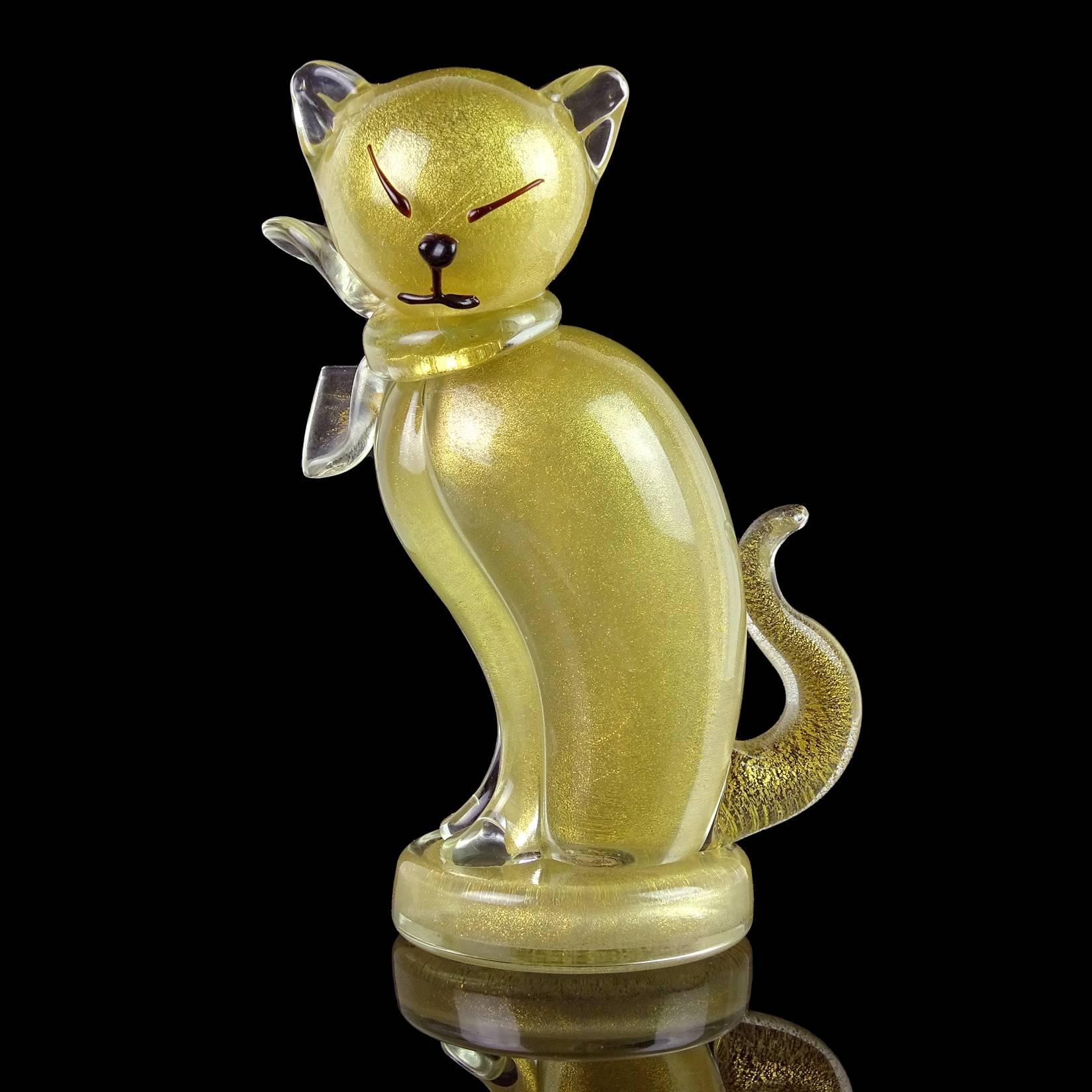 Beautiful vintage Murano hand blown clear and gold flecks Italian art glass kitty cat sculpture on round base. Documented to designer Alfredo Barbini. The piece is profusely covered in gold leaf, with bow around its neck. Stands on a round disk, and