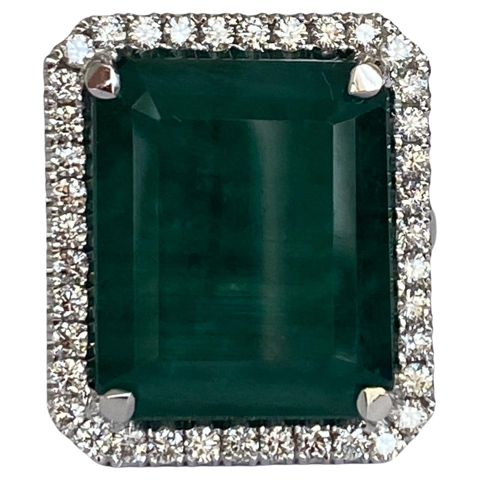 Offered in new condition, an 18 carat handmade white gold ring with a natural emerald cut emerald of 12.64 crt in the center, surrounded by 39 pieces of brilliant cut diamonds totaling approximately 0.65 crt of quality G/VS/SI. The color of the