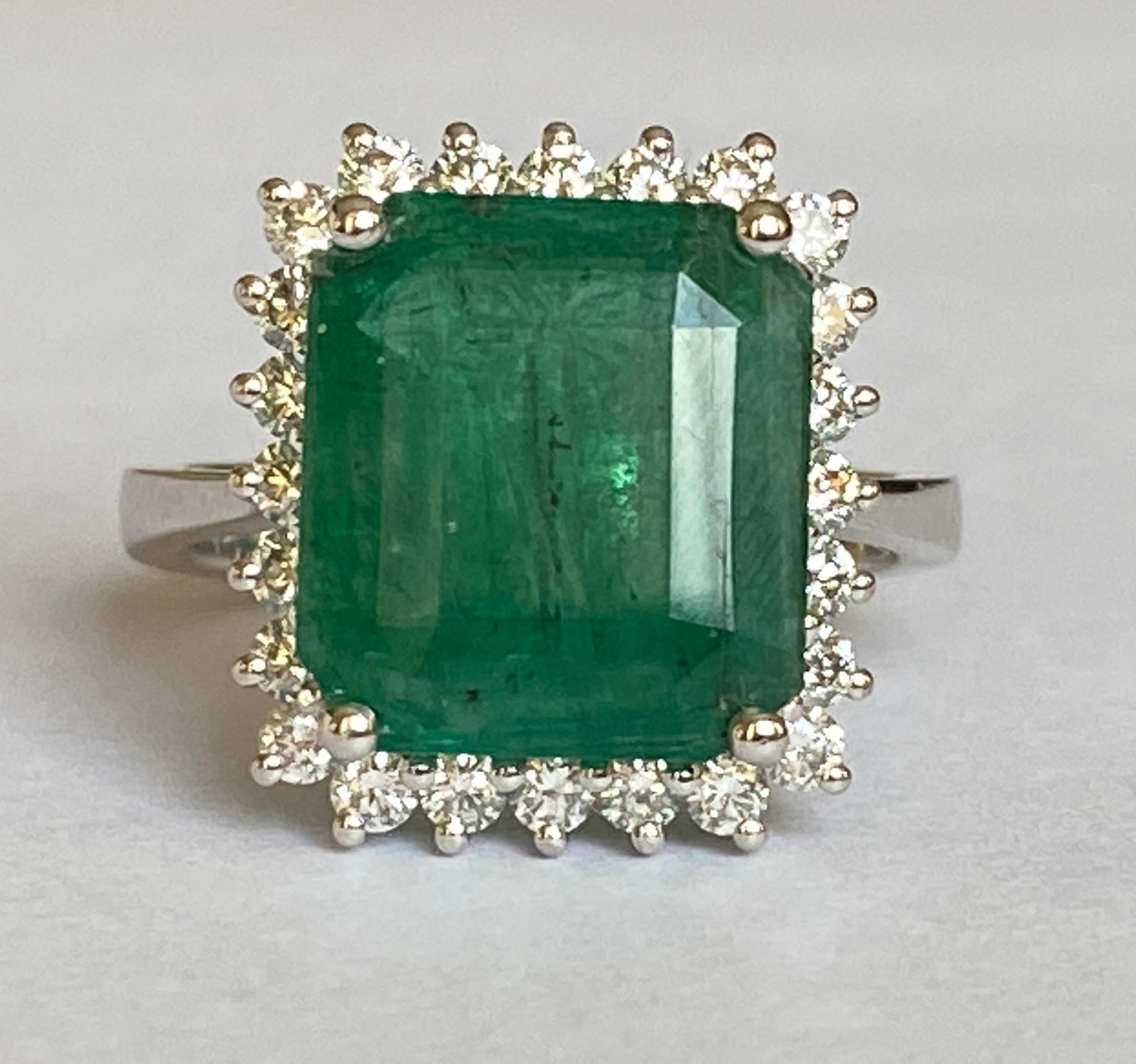 Offered in new condition, an 18 carat white gold ring with a natural emerald step cut emerald of 6.11 crt in the center, surrounded by 24 pieces of brilliant cut diamonds totaling approximately 0.48 crt of quality F/G/VS. The color of the emerald is