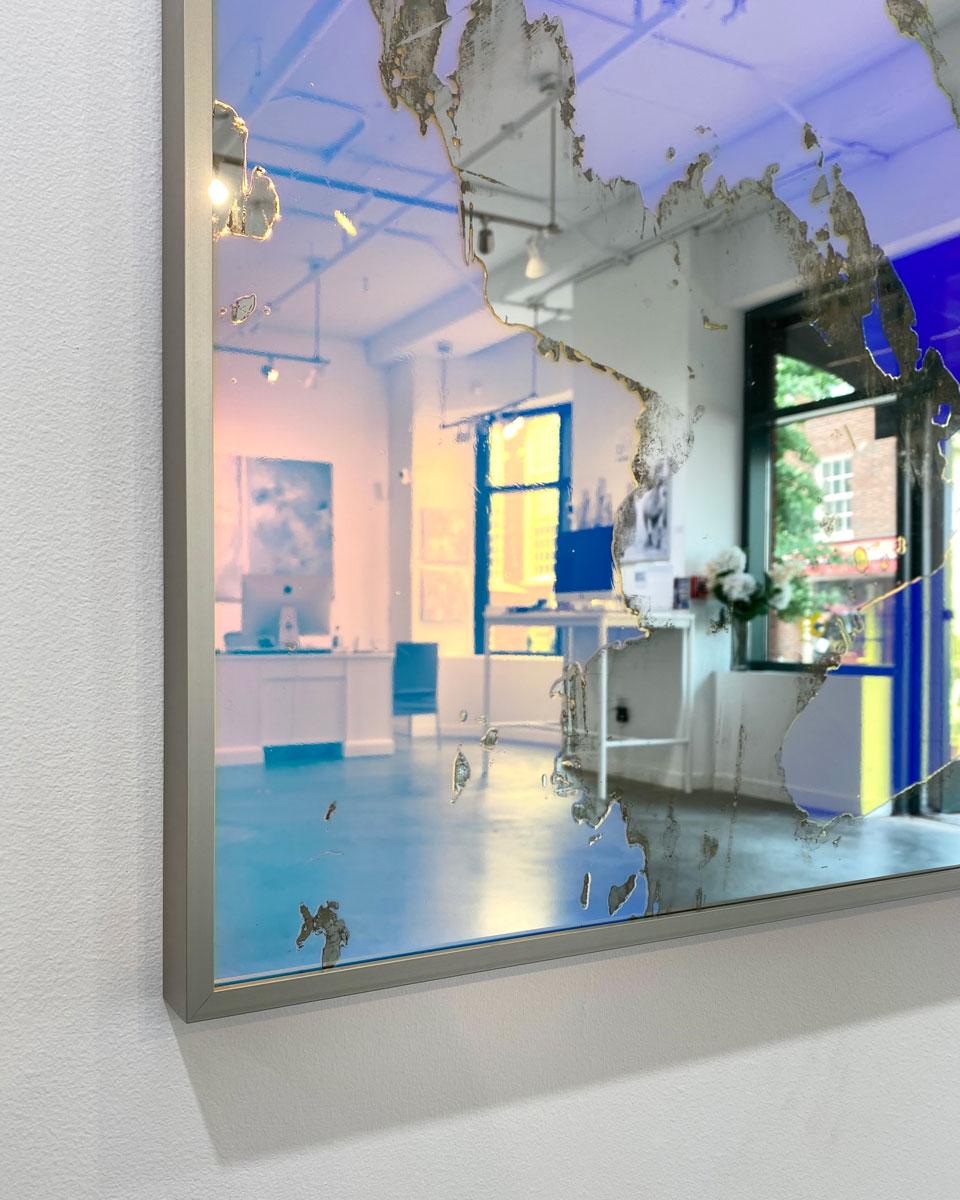 Dieser große abstrakte Kunstspiegel von Alina B ist mit dichroitischer Folie auf Spiegel gefertigt und in einen champagnerfarbenen Rahmen eingefasst. Die Folie auf dem Spiegel sorgt dafür, dass er und der Raum, den er reflektiert, je nach