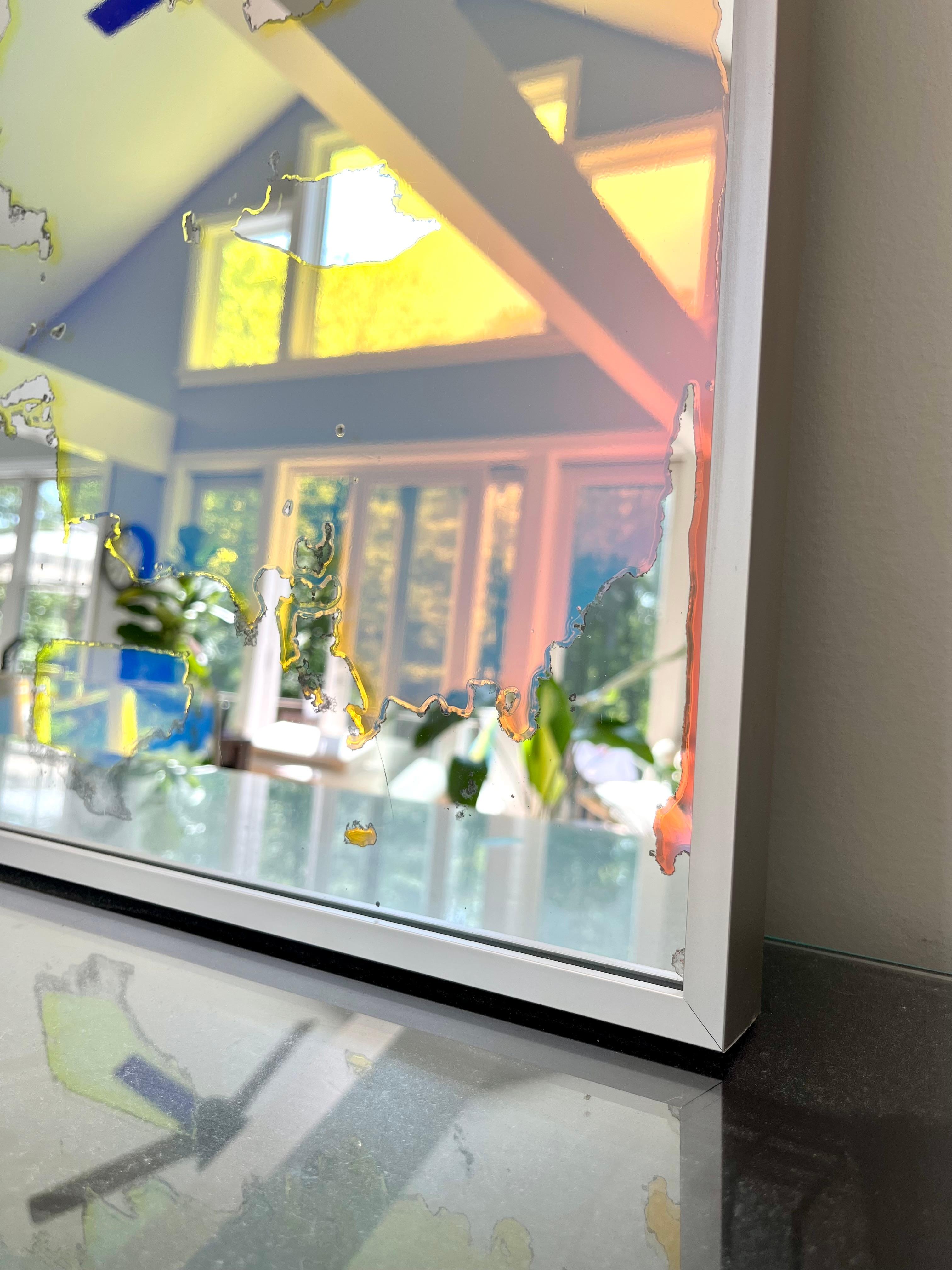 Ce miroir d'art abstrait d'Alina B est réalisé avec un film dichroïque sur miroir, et est encadré dans un cadre aux tons champagne. Le film sur le miroir permet à celui-ci, ainsi qu'à l'espace qu'il reflète, de sembler changer de couleur en fonction
