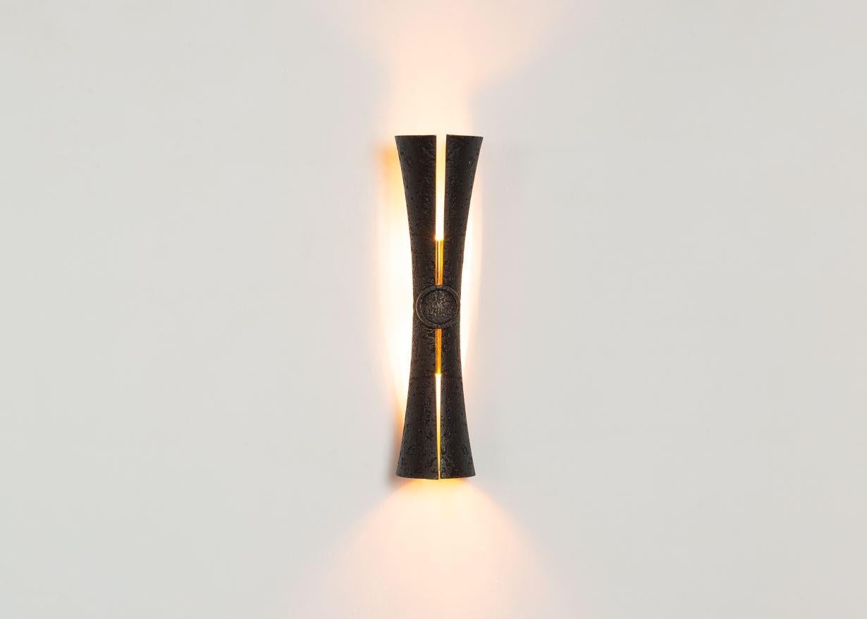 Cinched at the waist and split delicately along its length to reveal a polished bronze interior and, when illuminated, a ribbon of light, this shapely wall lamp reads as a graceful reinterpretation of the sconce. Designed to add a touch of theatre,