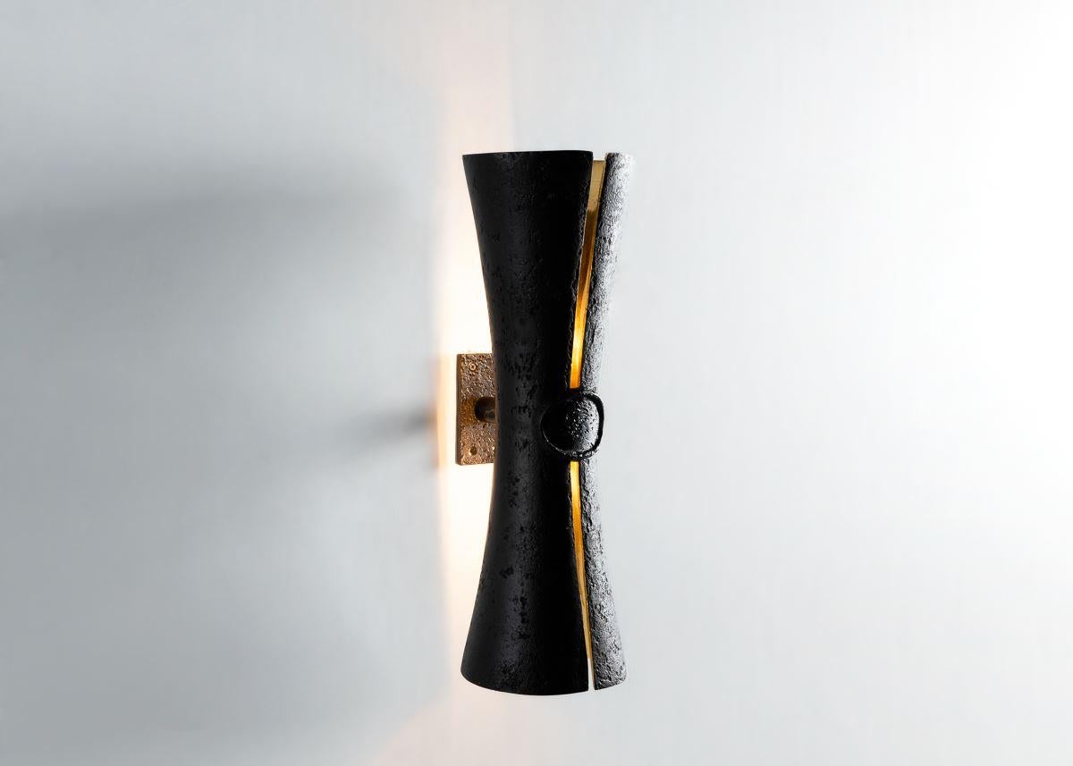 Cinched at the waist and split delicately along its length to reveal a polished bronze interior and, when illuminated, a ribbon of light, this shapely wall lamp reads as a graceful reinterpretation of the sconce. Designed to add a touch of theatre,