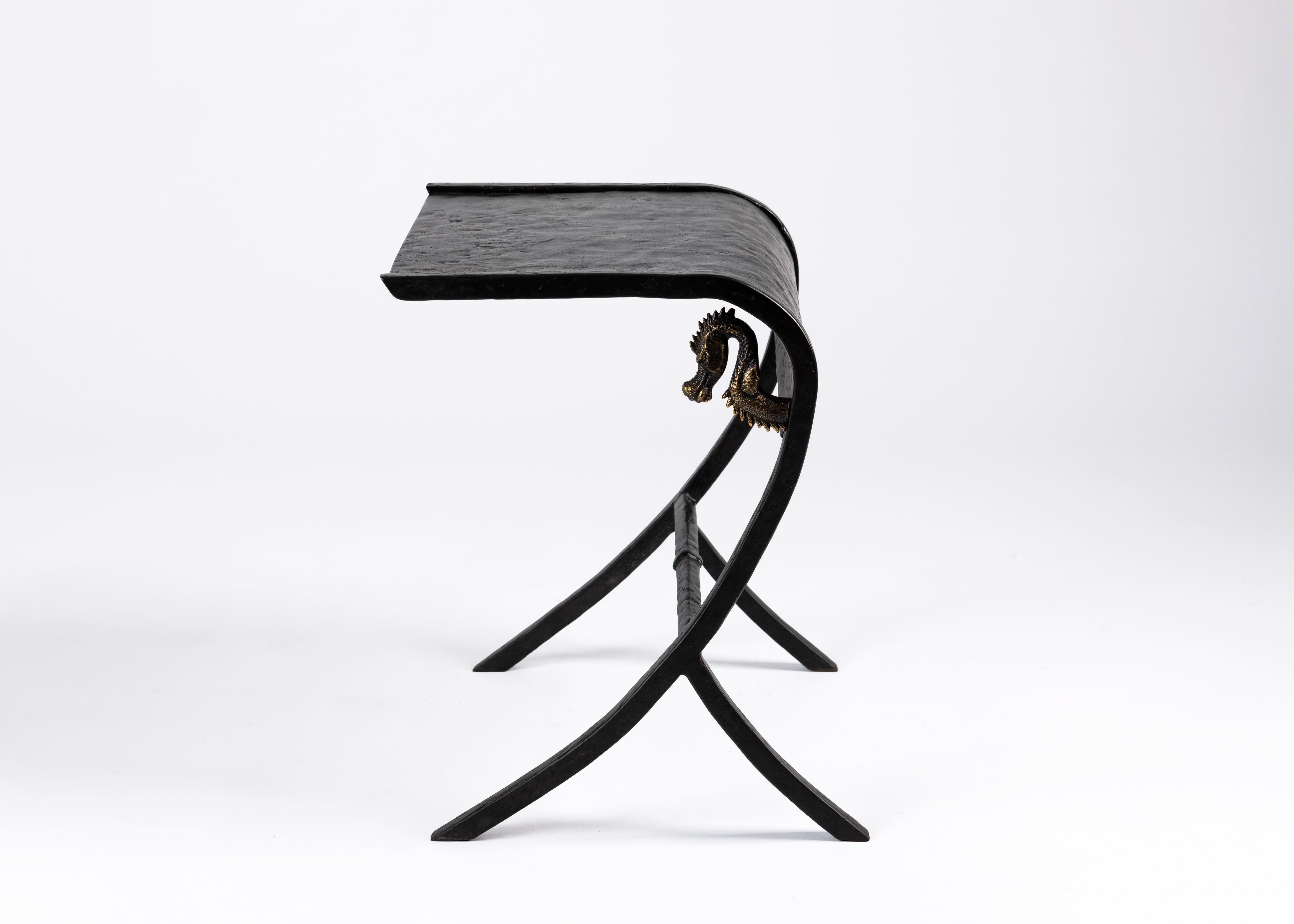 Deux bandes parallèles de bronze patiné se courbent sinueusement vers le sol et sont soutenues par l'arrière pour former le cadre d'une table d'appoint texturée qui peut facilement être placée à côté d'un canapé. La courbe intérieure est ornée de