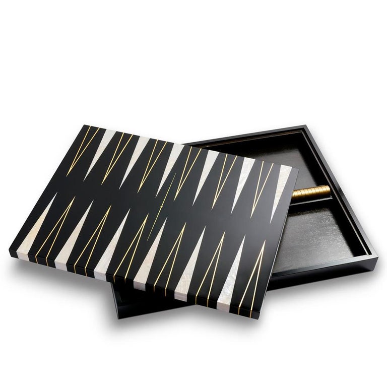 Backgammon all black with wooden frame
in solid wood in black lacquered finish. With
black wooden lacquered top with white parts
in natural shell and with gilded trims. Including
tokens made in black resin with polished brass
shape and with