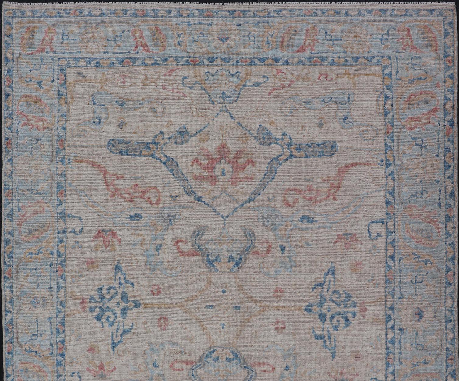 Hand knotted Oushak made in wool with a field is backed by a ivory color, with a light blue border, etched with elegant golden/brown branches. The arabesque-like design brings splashes of light blue, cognac, and reddish brown color. 

Measures: