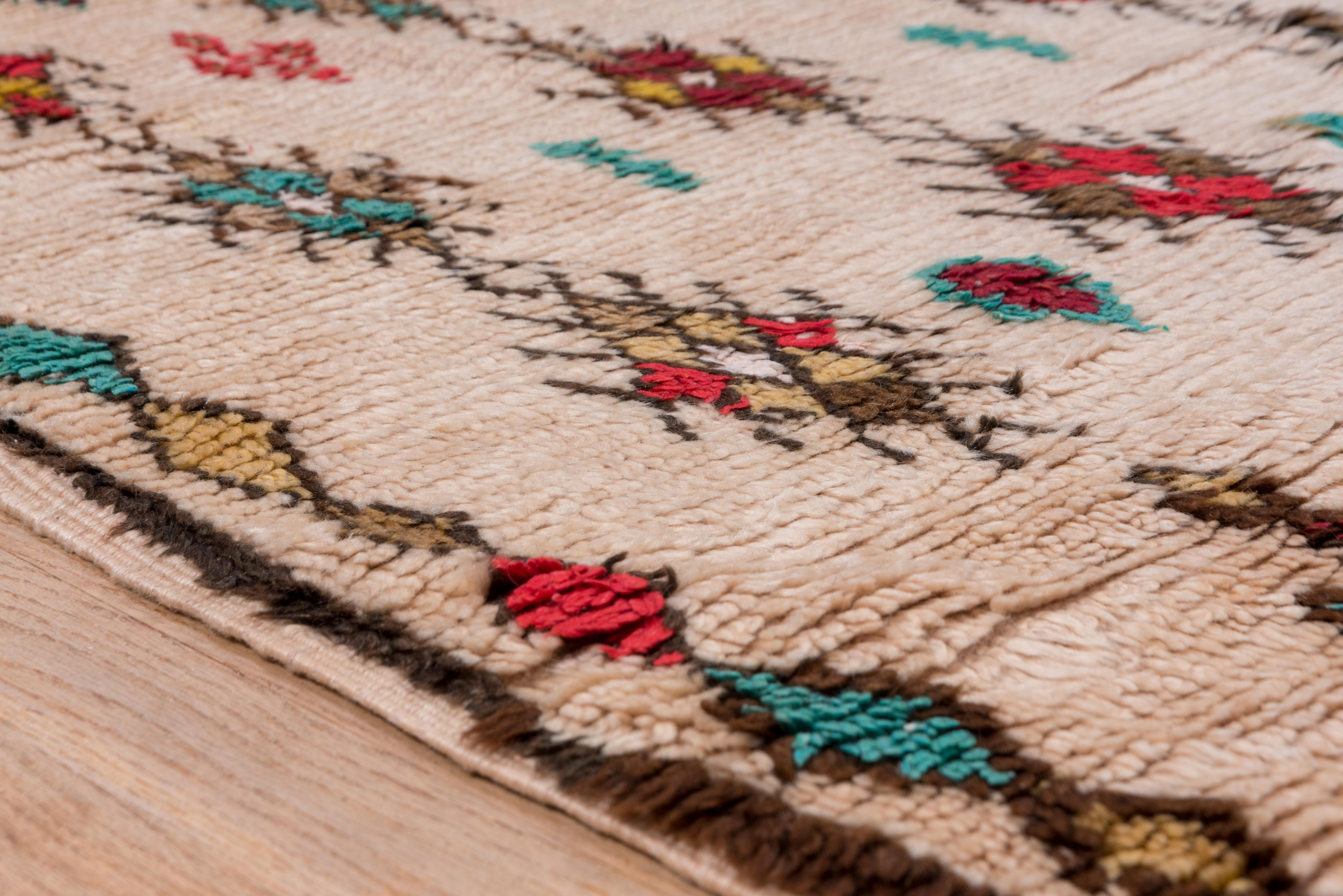 Marokkanischer Dorfteppich mit einem All-Over-Medaillon-Motiv. Helle, kräftige Farben werden durch die traditionelle cremefarbene Wolle kontrastiert, die die Basis des Feldes für dieses Stück bildet. 