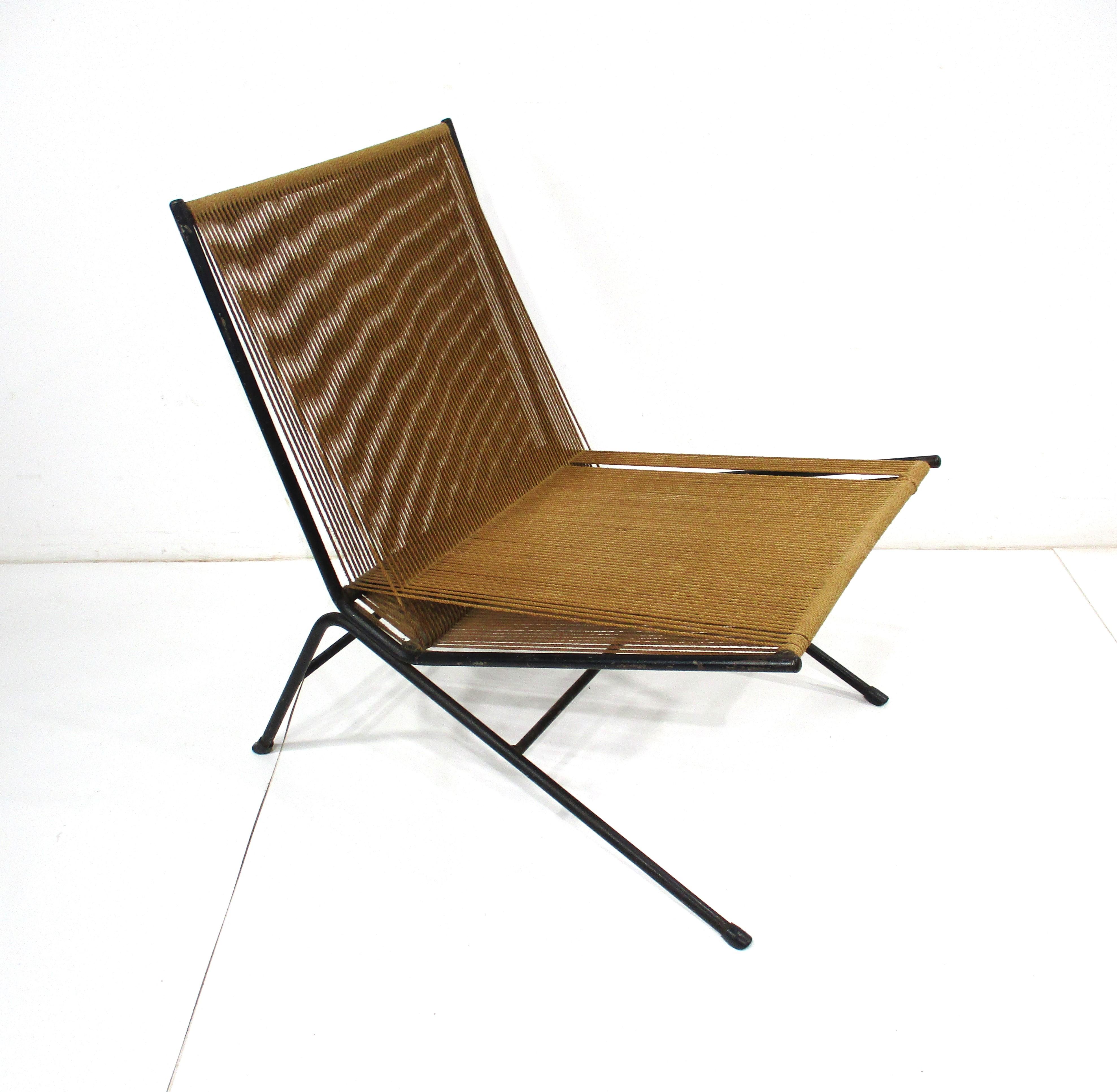 A angled sculptural black iron framed Mid Century lounge chair with string woven back and seat bottom . Designed by Allan Gould in the 1950's it brought together two really different materials being heavy iron and light woven rope string . Before