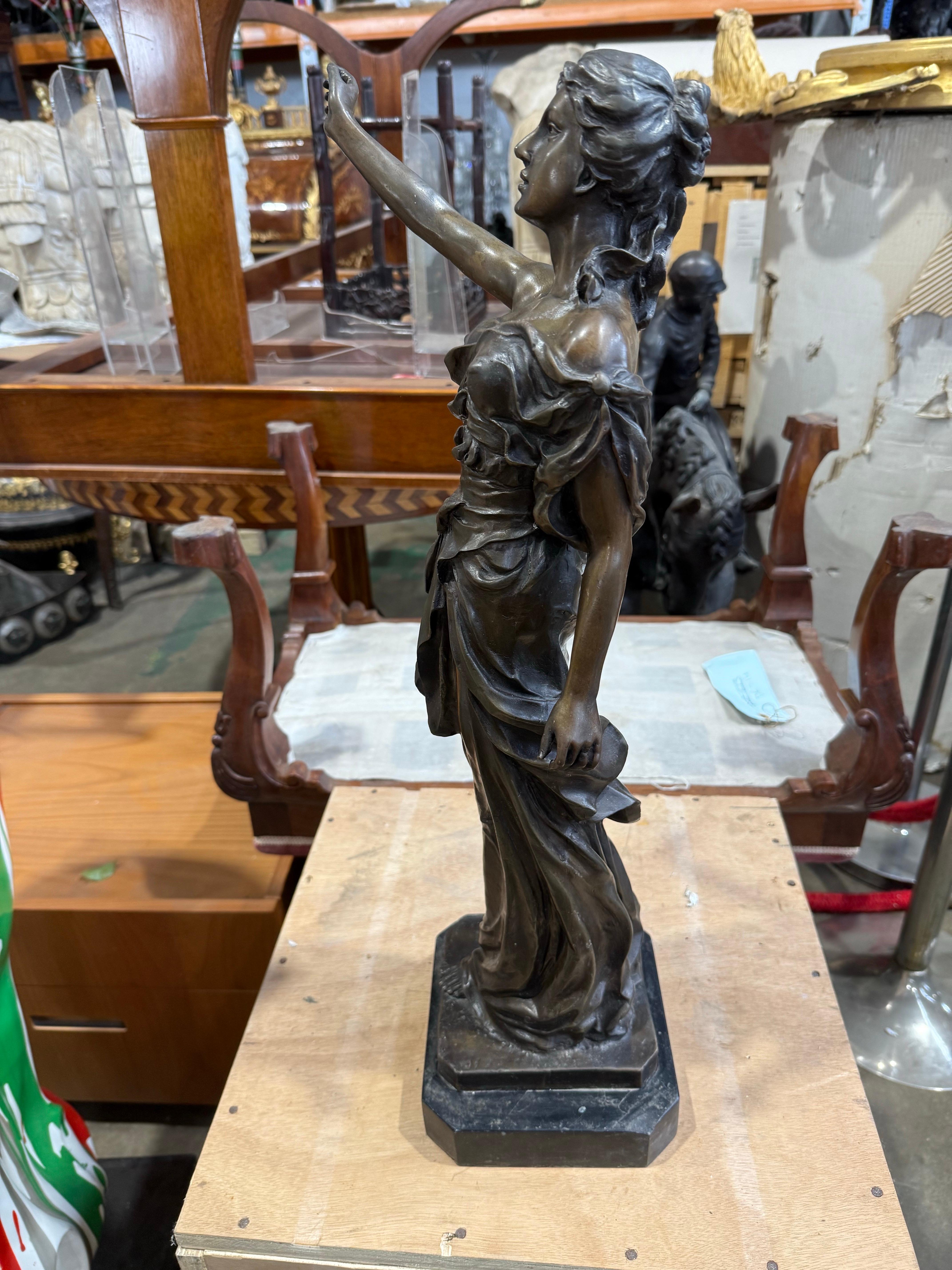 An evocative early 20th century bronze allegorical sculpture depicting a robed female figure in a commanding stance, arm extended skyward in a powerful gesture of inspiration or triumph. Dressed in flowing classical drapery, she stands barefoot on a