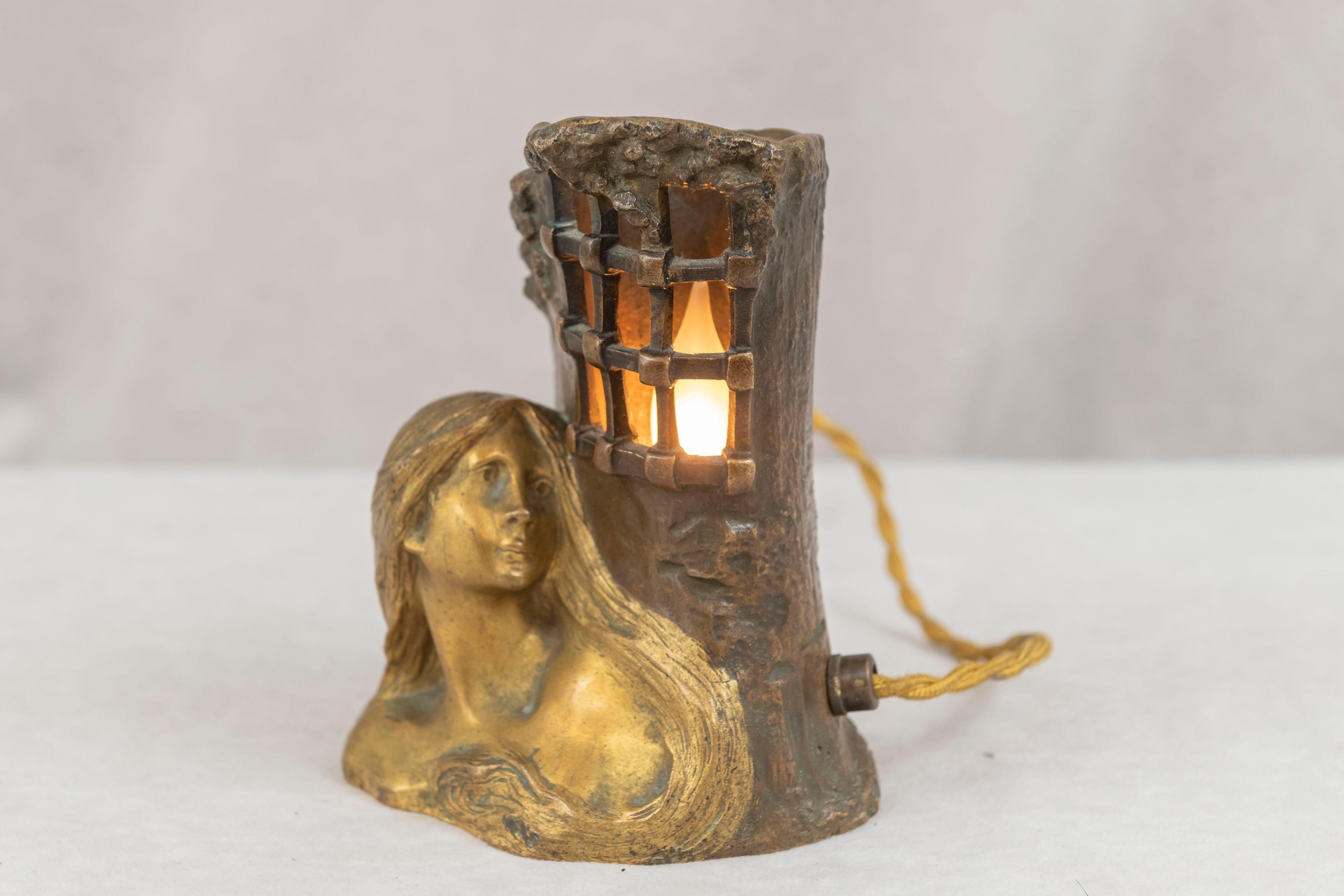  This lovely little lamp depicting a gilt bronze bust of a maiden looking into a stone room with bars certainly is an allegorical tale. Her distinct rich free flowing hair commands your attention. The room does light up and creates an interesting