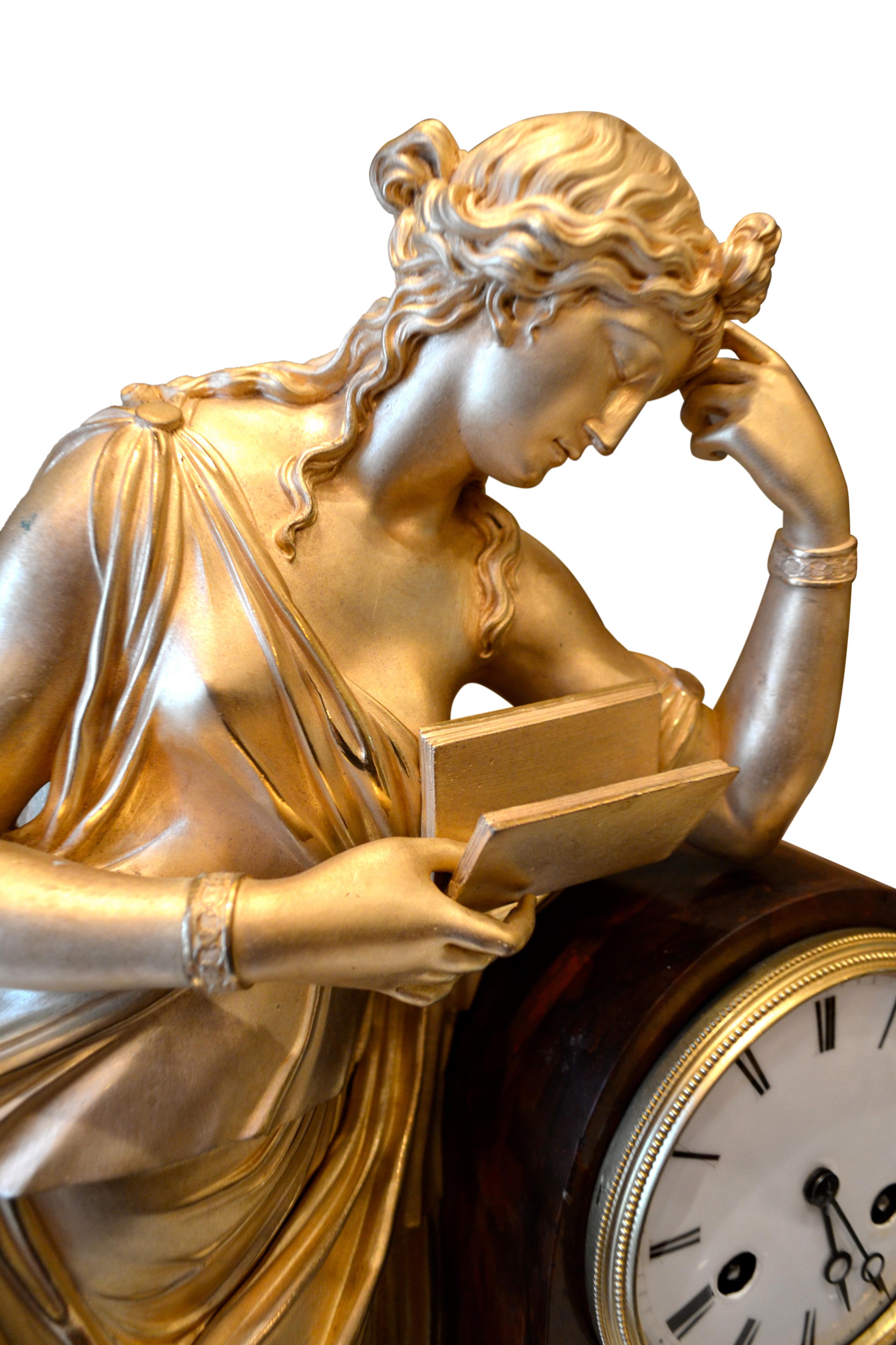 A French Louis Philippe allegorical gilt bronze and marble mantle clock depicting Clio, The Greek Muse of History. The standing figure of a gilded Clio is shown leaning against the clock plinth reading a book with one hand, the other hand bent to