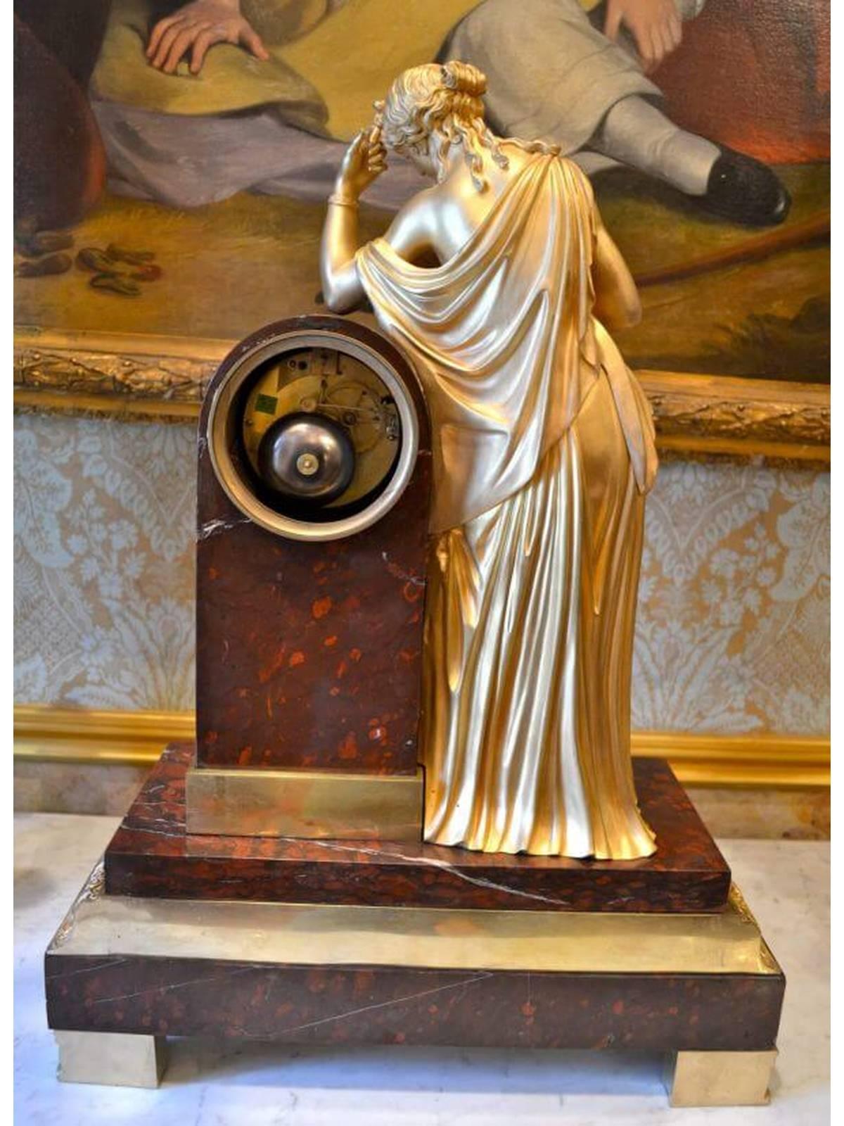 A large late French Empire gilt bronze and marble mantle clock. The standing figure of a gilded Clio leans against the clock plinth reading a book with one hand, the other hand bending to support her head. The figure and plinth sit upon a stepped