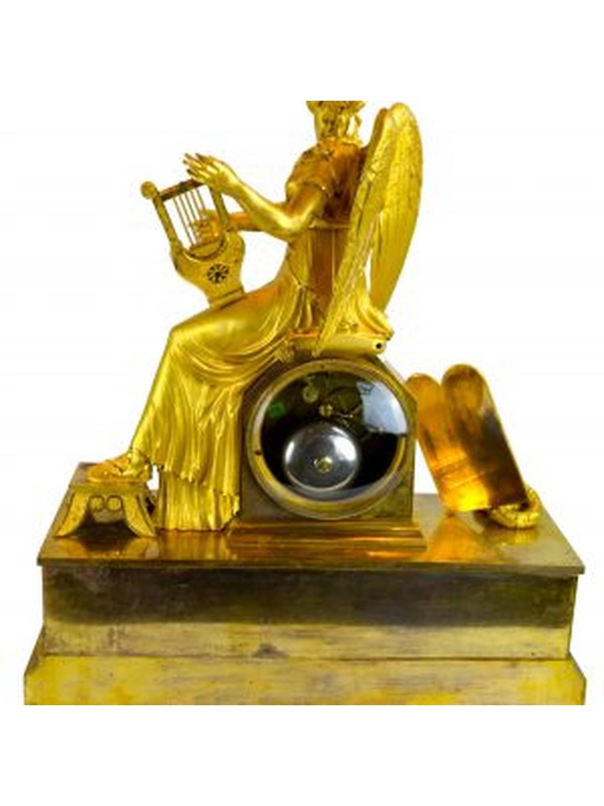 Clio, the muse of history and music, is shown here sitting on the clock plinth playing her harp. To the left of the clock dial are placed wreaths, and a plaque with the names Pline, Homere, Tasse, and Virgile. The lower section of the clock is