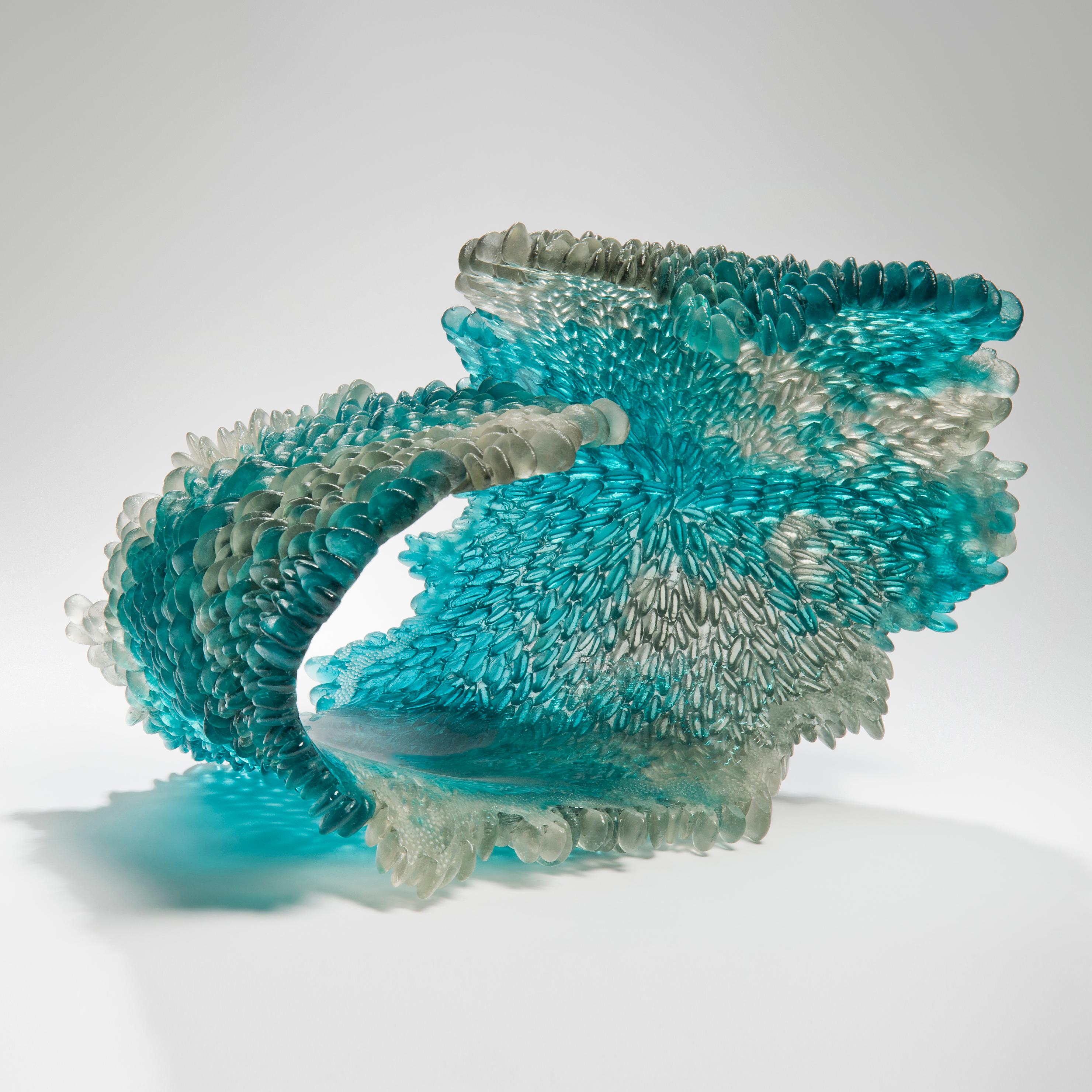 Alliform II is a unique textured glass sculpture in clear and teal by the British artist Nina Casson McGarva. 

Casson McGarva firstly casts her glass in a flat mould where she introduces all of the beautifully detailed, scaled surface texture,