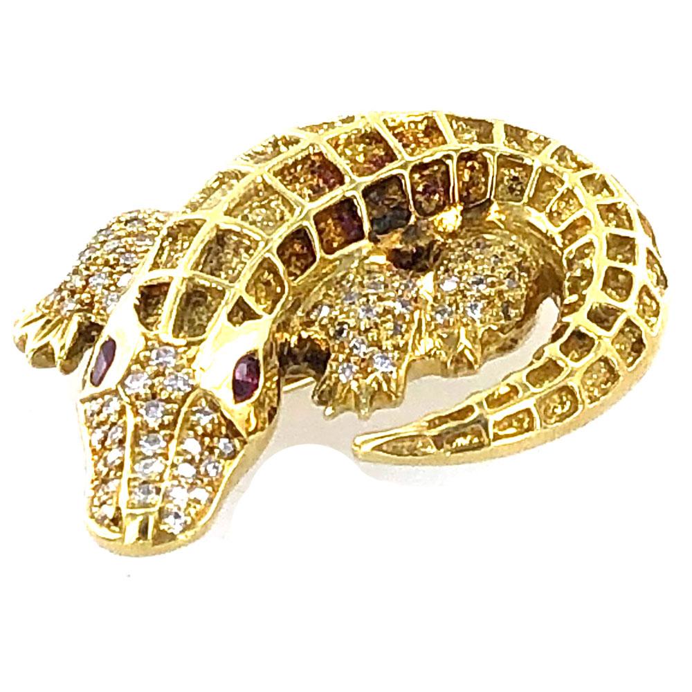 Adorable 18 karat yellow gold alligator pin fashioned in 18 karat yellow gold. The solid and textured brooch features 84 round brilliant cut diamonds that equal approximately 1.00 carat total weight. The alligator has ruby red eyes, and measures 1.5