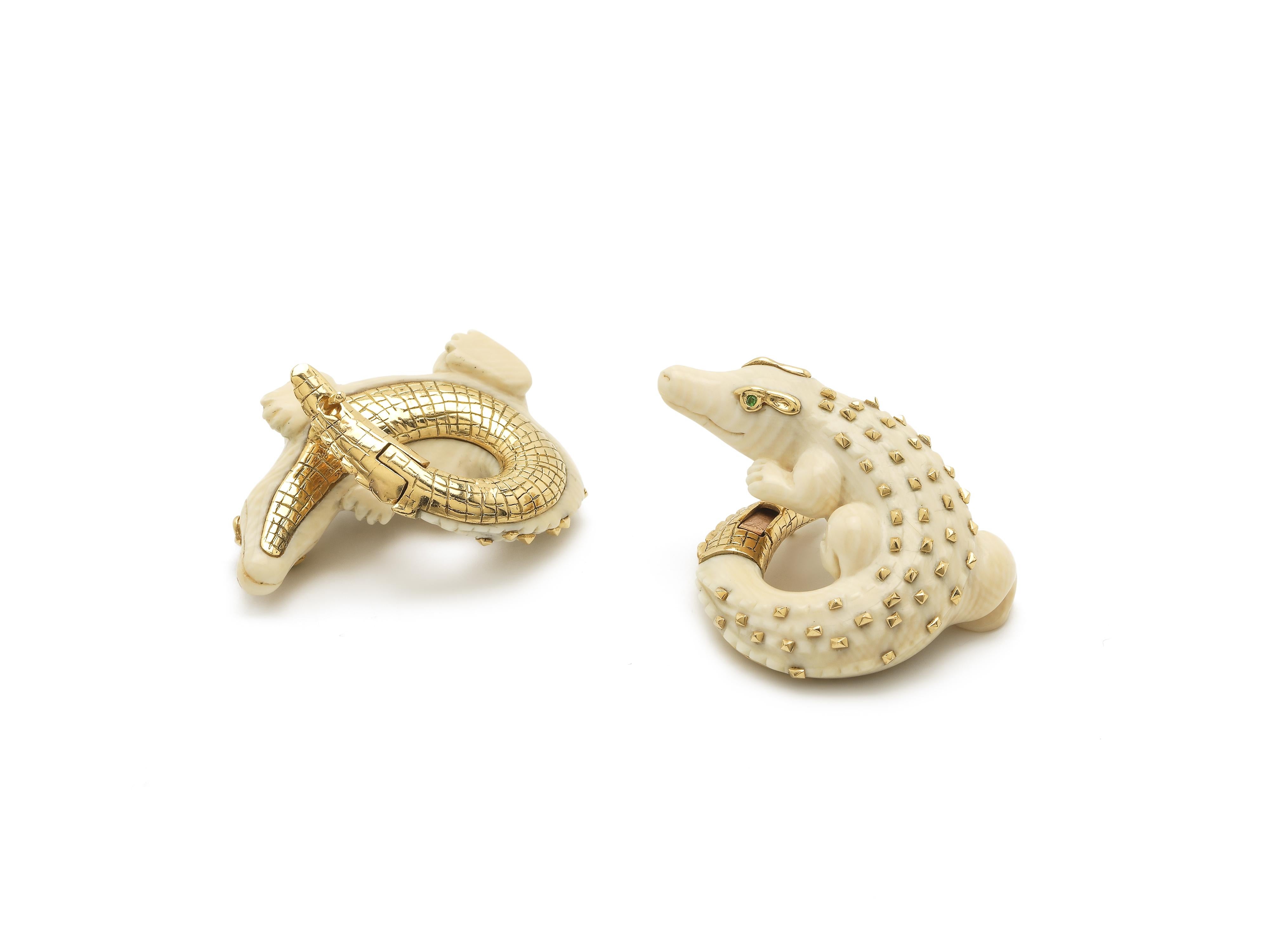 Two playful alligators, carved in 60,000-year-old mammoth tusk, are crafted to coil around the lobe in these bold earring designs. Fashioned with 18k yellow gold embellishments on their bodies and green tsavorite eyes, the earrings’ closing