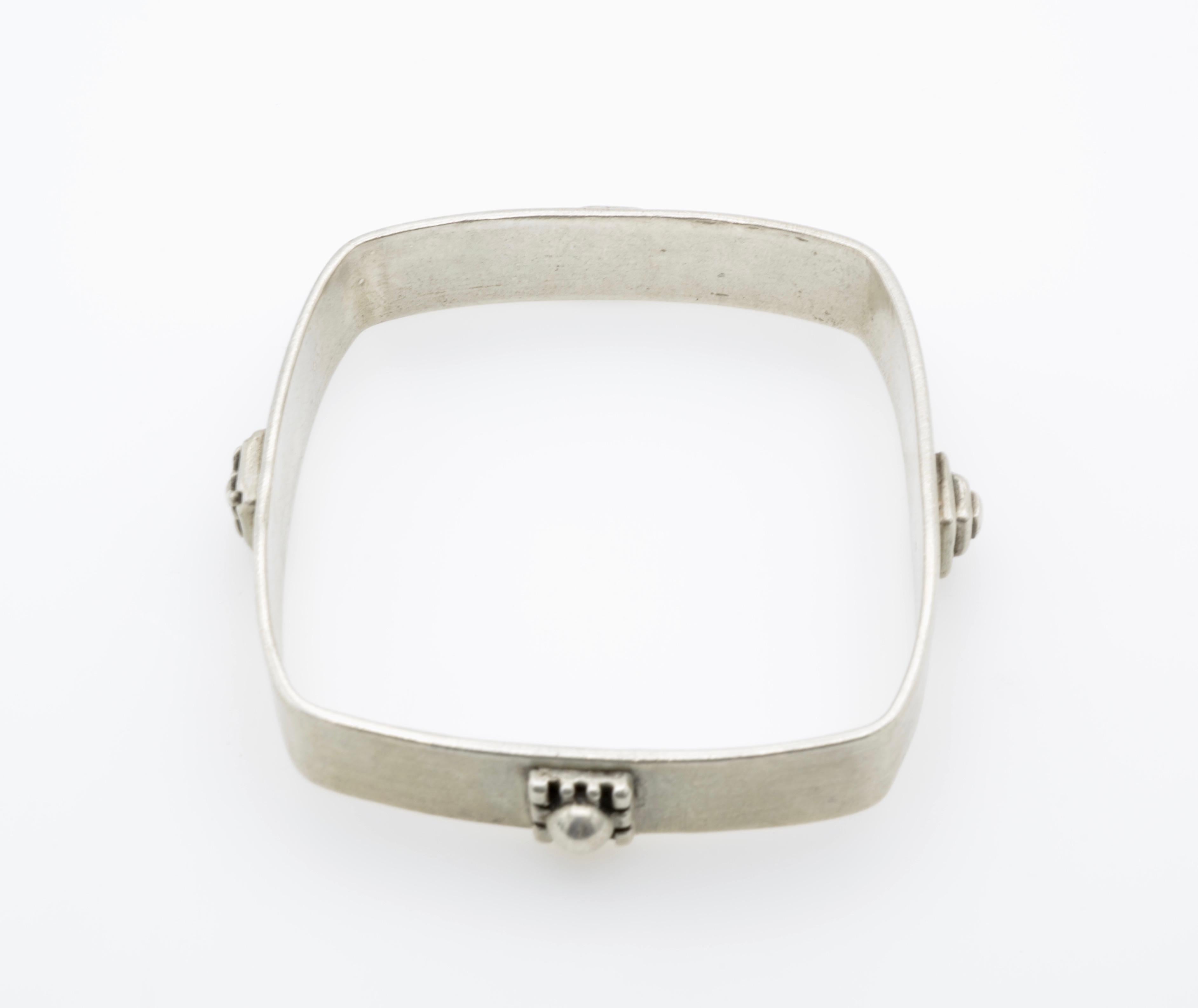 This beautiful square bangle created by Allison Stern is in a bright white sterling silver with four different square adornments on each side. She has a classic and unique style to architectural jewelry design and spent plenty of time studying in