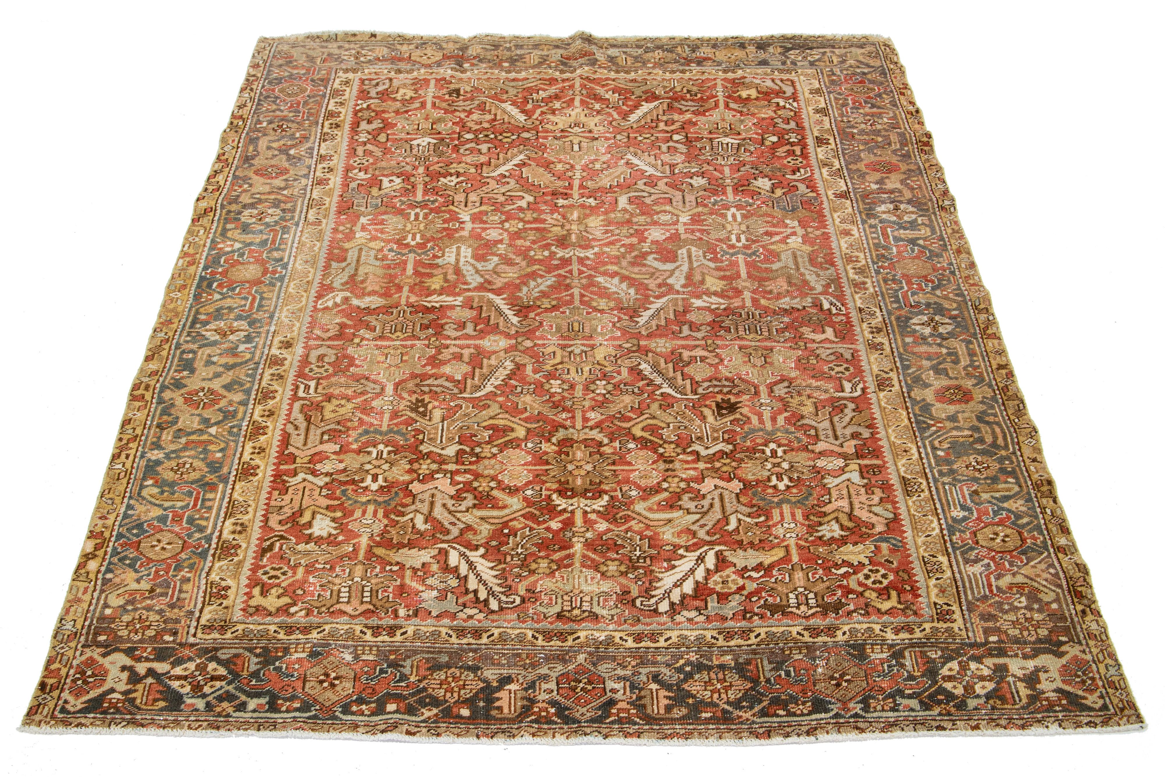 This antique Persian Heriz rug is crafted with hand-knotted wool. The rust-colored field features an allover design embellished with shades of peach, gray, and brown.

This rug measures 7'10