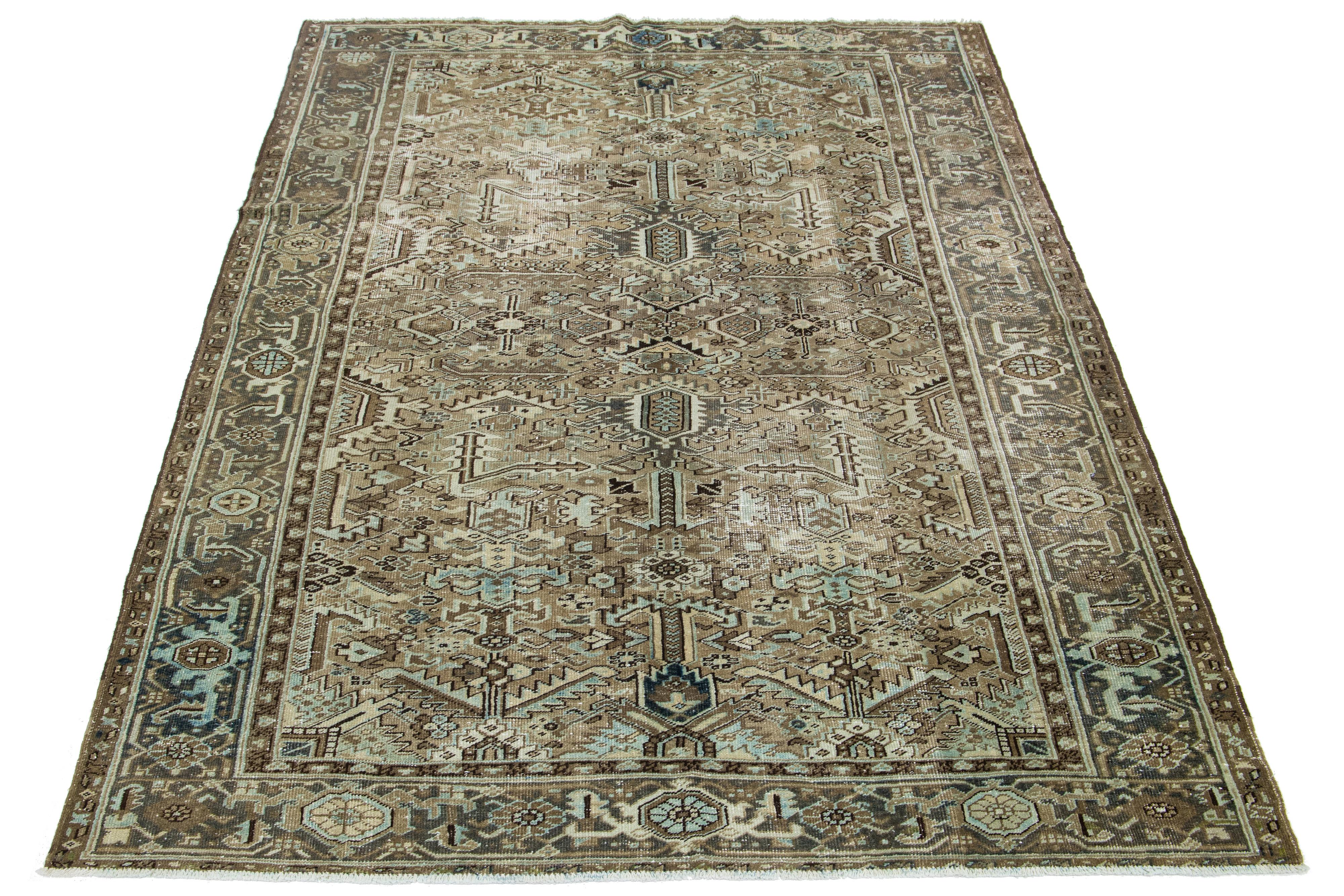 This antique Persian Heriz rug is crafted with hand-knotted wool. The brown-colored field features an allover design embellished with shades of blue and beige.

This rug measures 7' x 10'2
