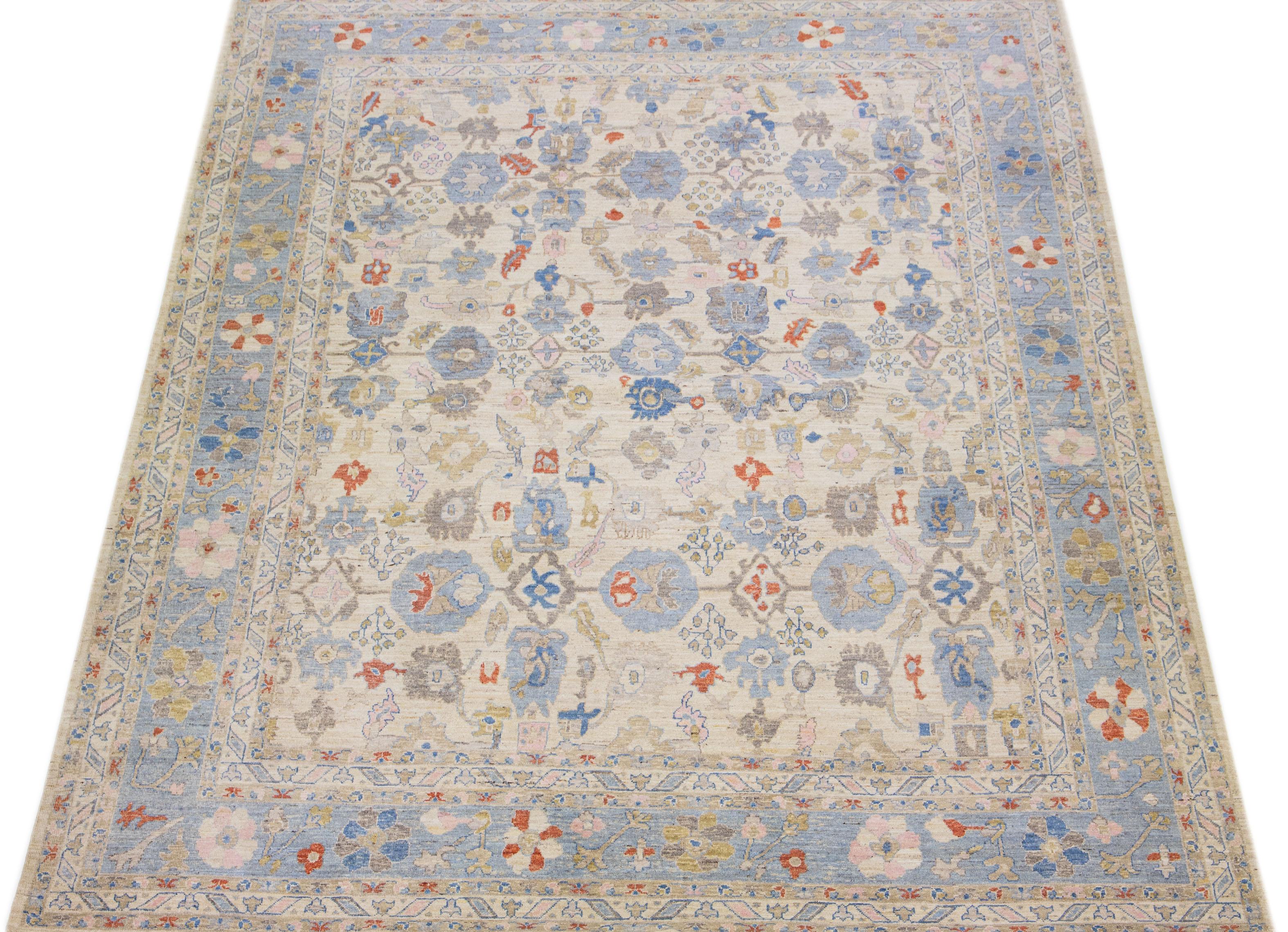 This hand-knotted wool rug showcases an exquisite modern Oversize Sultanabad design in a stunning beige color palette. Its intricate blue frame features captivating accents in rust, blue, and pink hues arranged in a remarkable all-over