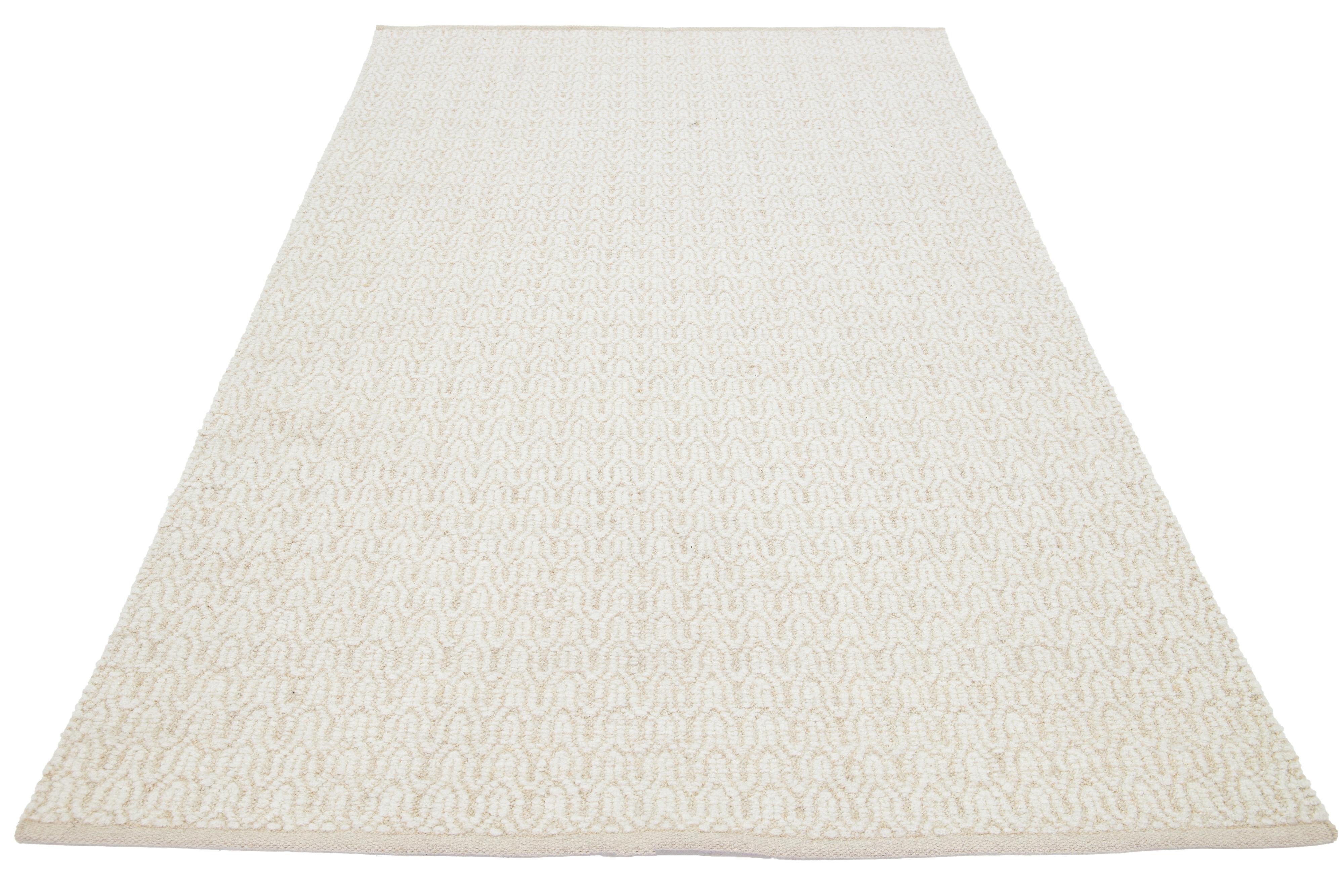 Questo bellissimo tappeto in lana lavorato a mano dalla texture moderna, che fa parte della nostra collezione Sasco, presenta un campo di colore beige con accenti in avorio. Il tappeto vanta anche uno splendido disegno strutturato che ricorda i