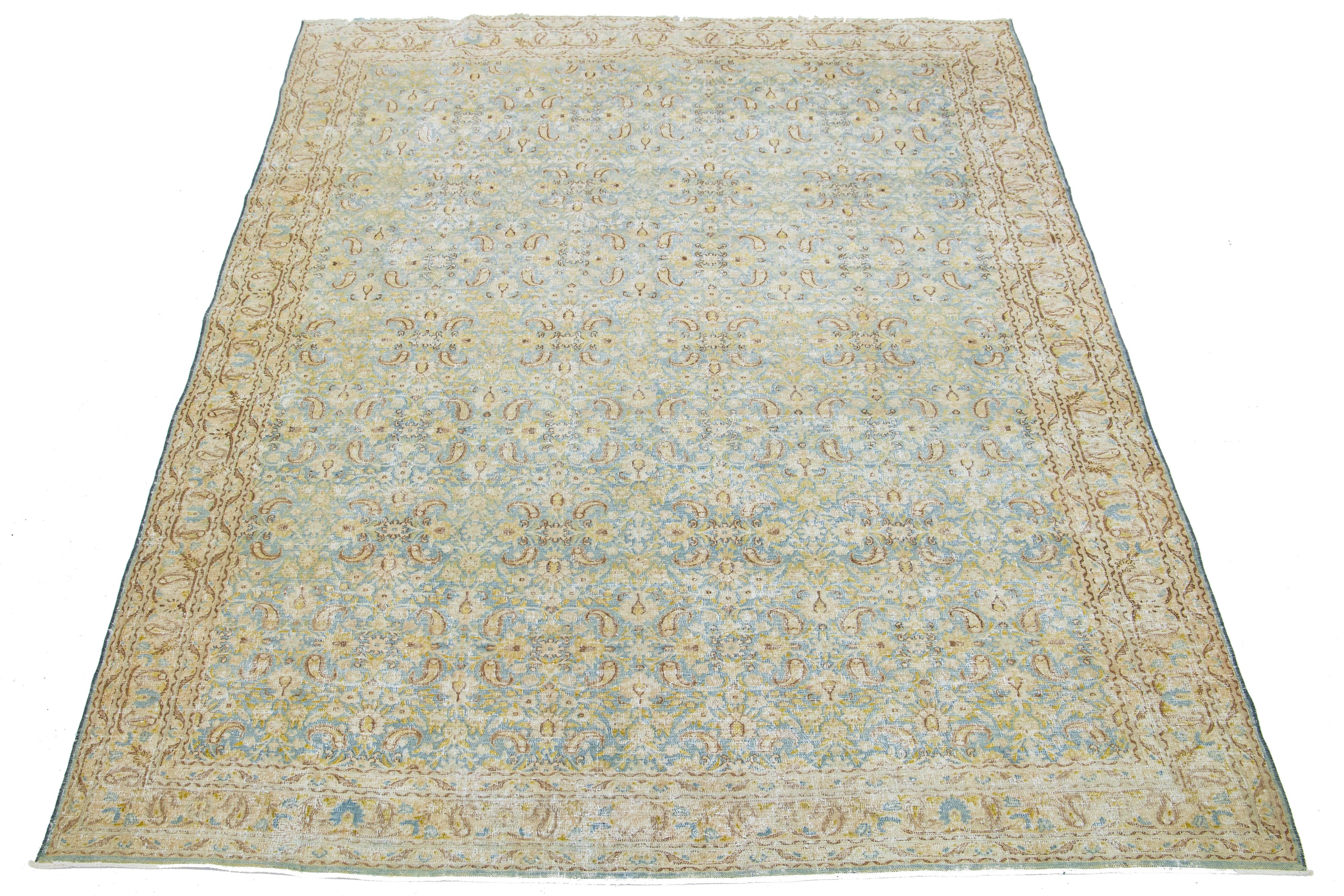 This Persian Tabriz wool rug from the 1920s showcases a handcrafted floral pattern. A contrasting light blue backdrop and beige, green, and brown colors accentuate the design.

This rug measures 6'8
