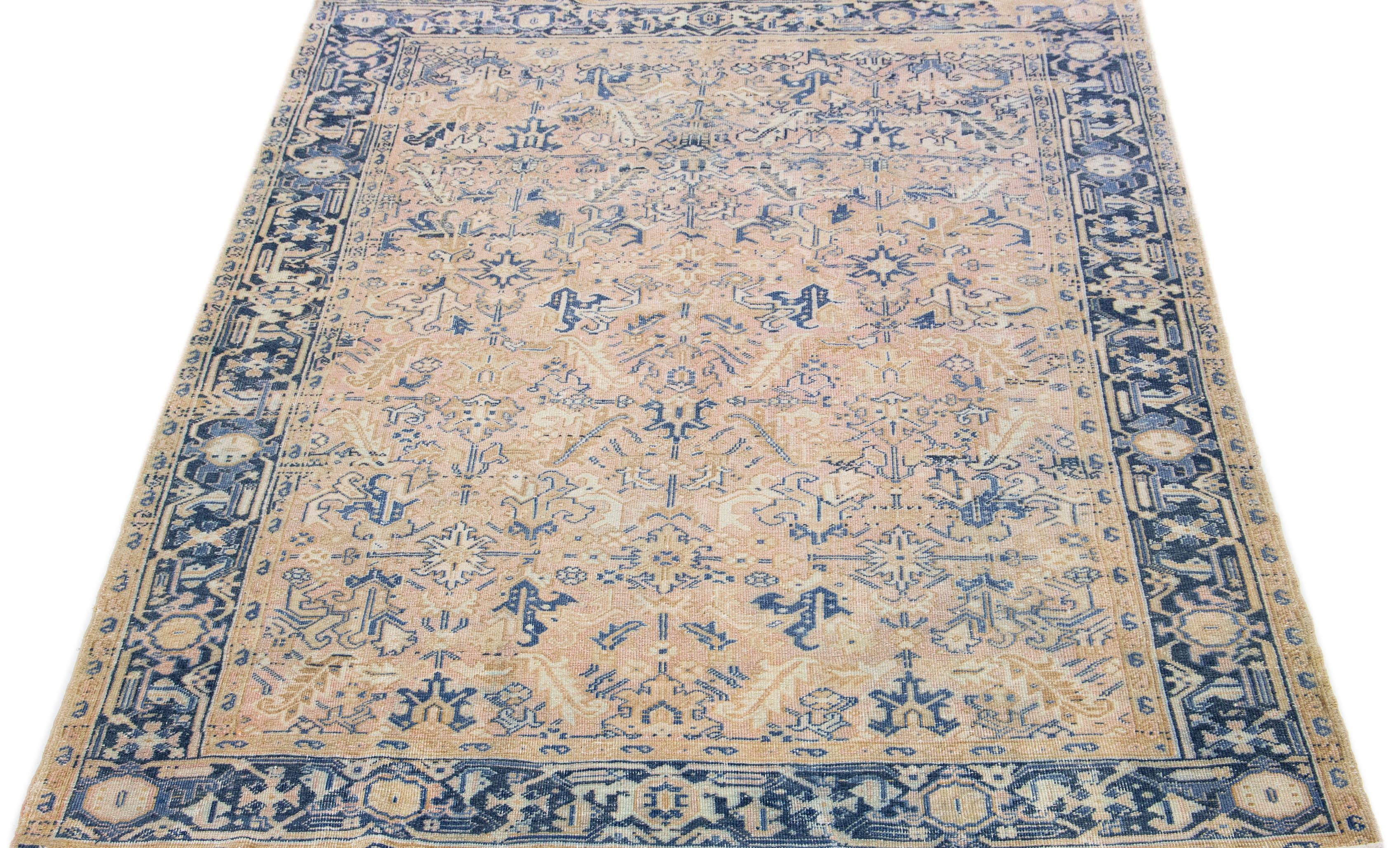 This Persian rug boasts a splendid all-over design with an eye-catching geometric floral pattern in shades of blue and brown set against a soft peach field. Using premium hand knotted wool, this antique Heriz rug radiates eternal class and