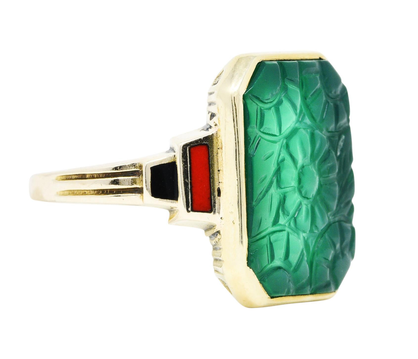 Octagonal ring is bezel set with a carved tablet of chrysoprase

Translucent bluish green in color and deeply carved to depict florals

With stepped shoulders glossed in orangey red and black enamel

Completed by deeply ribbed details at shoulder