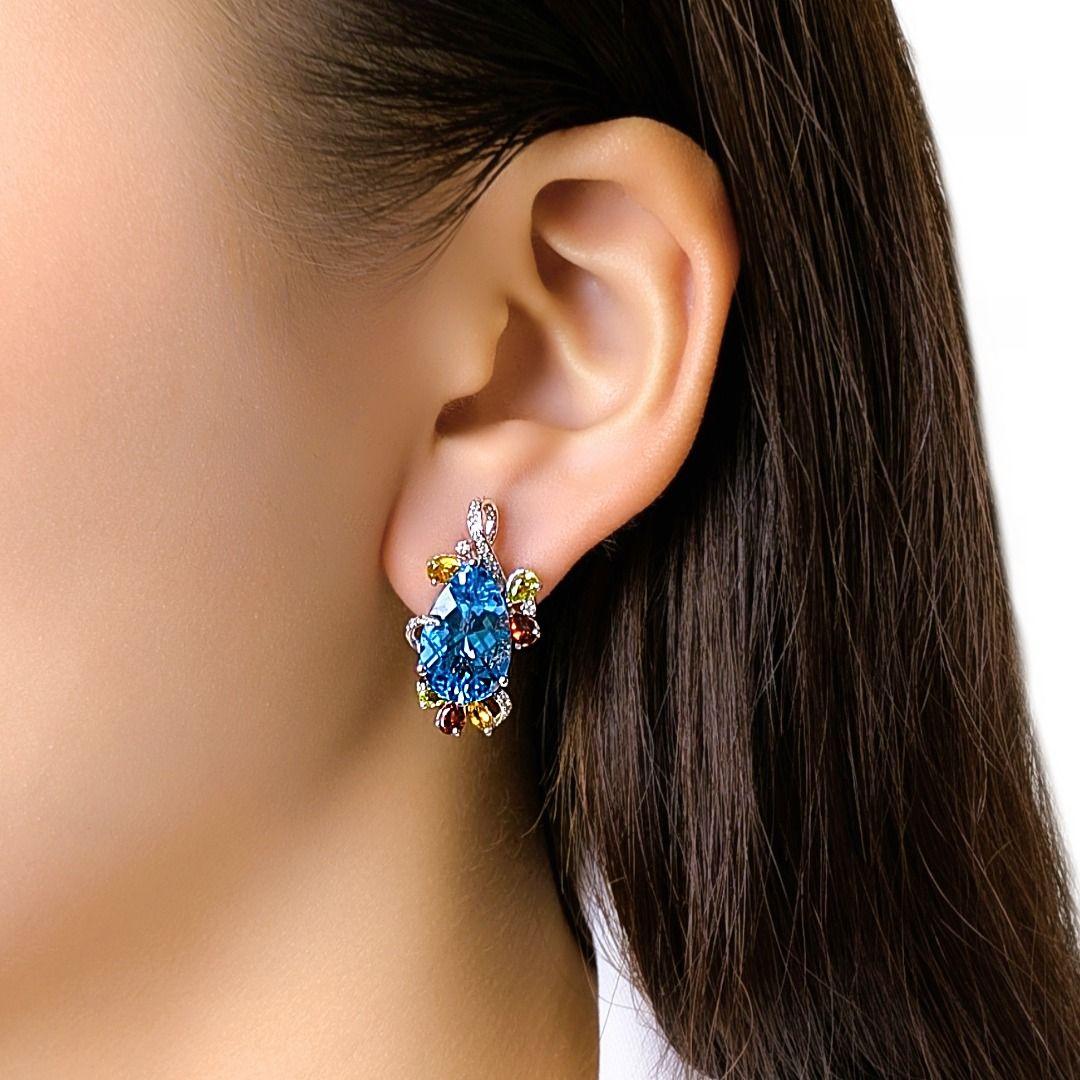 Ces boucles d'oreilles ornées présentent deux pierres centrales bleues en forme de poire, entourées de pierres mélangées multicolores aux riches teintes vertes, jaunes et rouges profondes, disposées dans une composition florale vibrante. Accentué