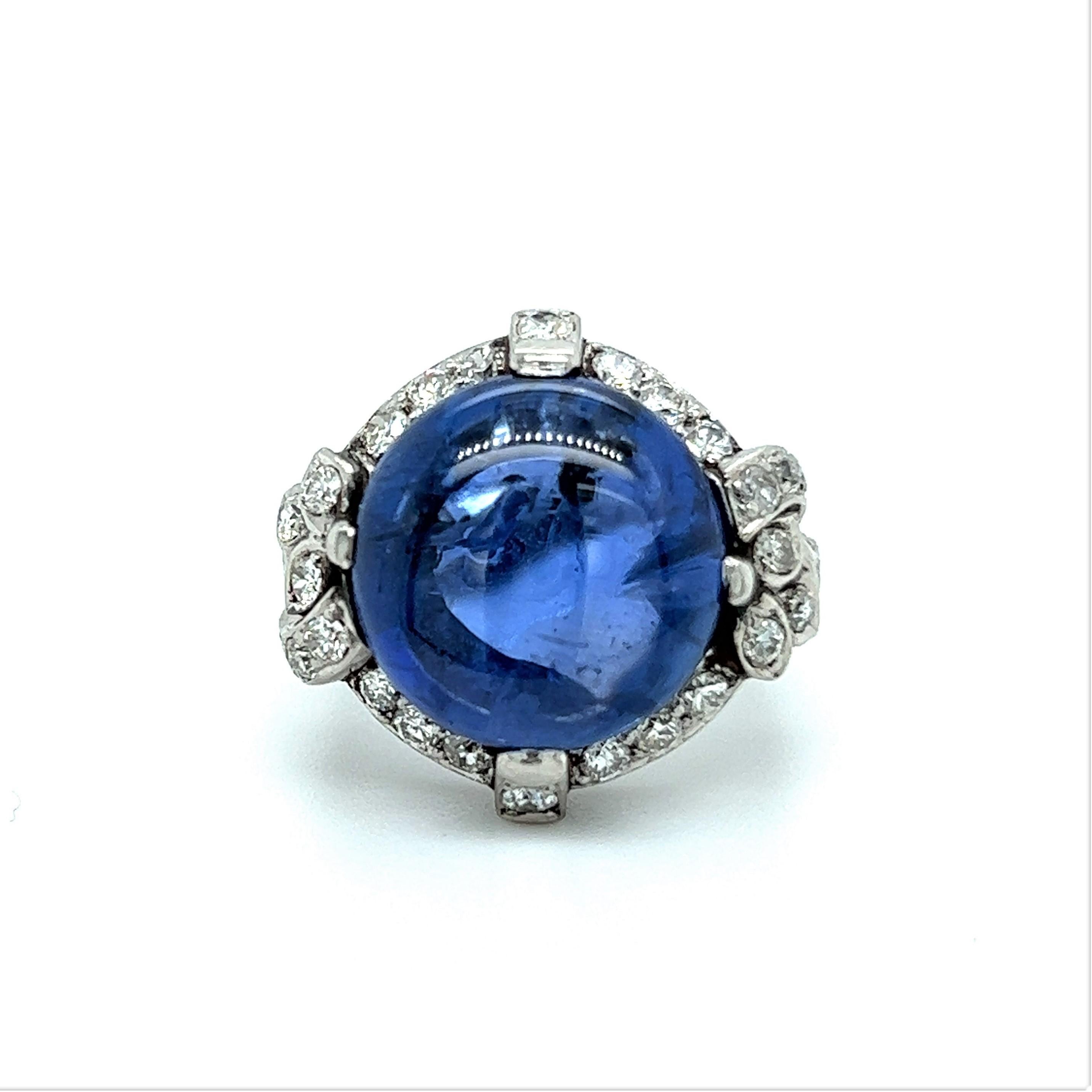 This outstanding antique ring is the embodiment of early 20th century glamour and sophistication. 
Center of the composition is a gorgeous, untreated, cabochon sapphire of approximate 15.20 carats. It is framed by refined platinum setting and 26
